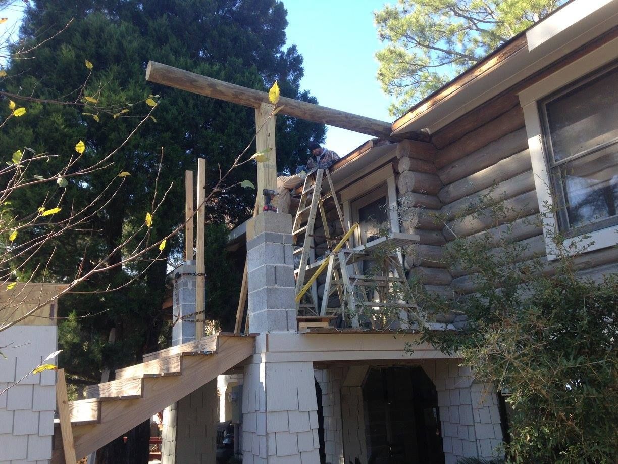 Construction in progress; unfinished porch with wooden stairs, supports, and a beam extending to the house.