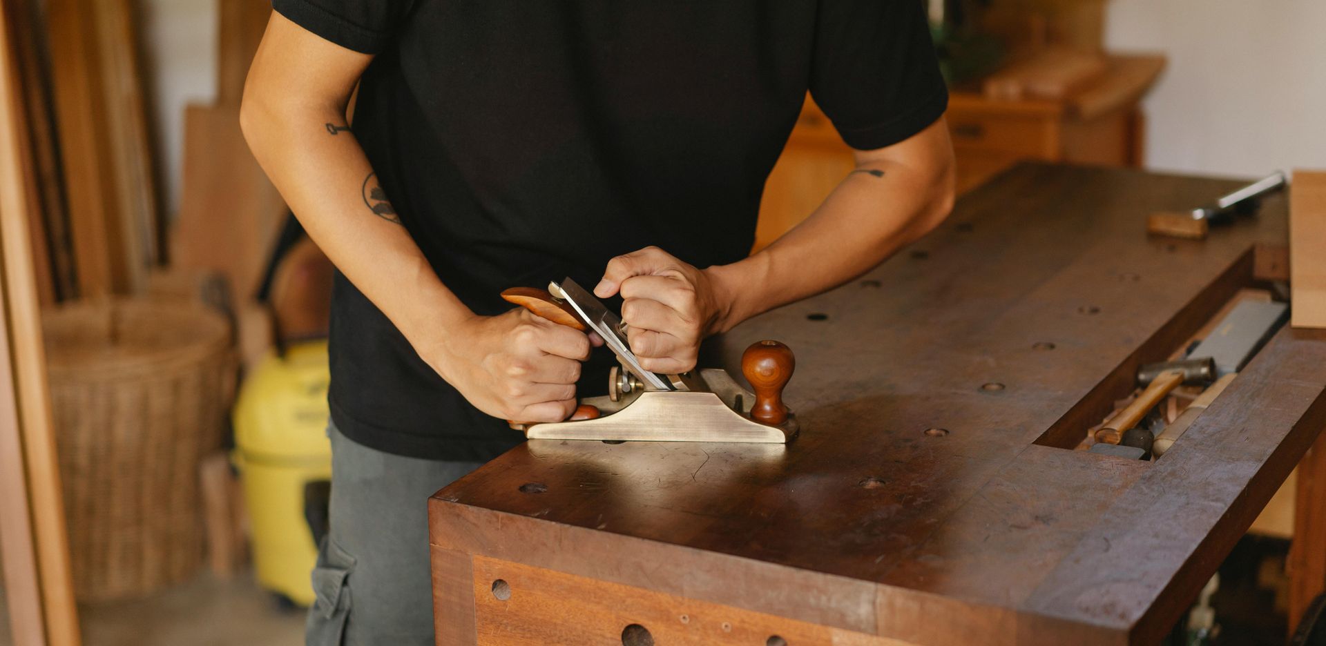 Person using a hand plane on a wooden workbench in a workshop.