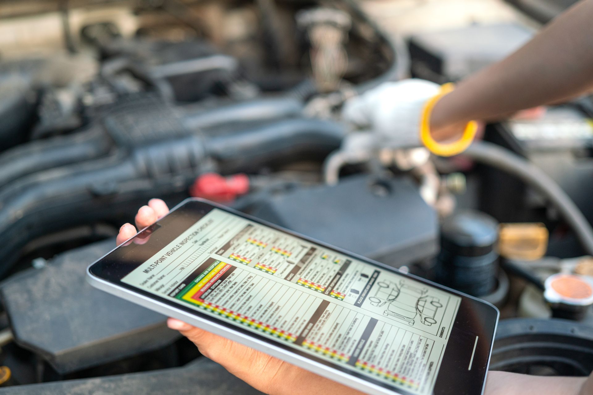 A person is holding a tablet in front of a car engine.