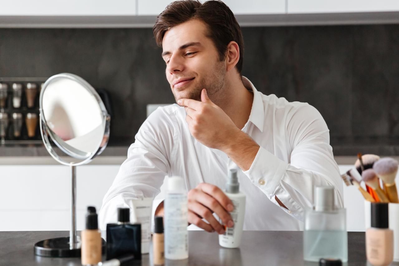 Homem em frente ao espelho com produtos de beleza em momento de autocuidado e skincare masculino.