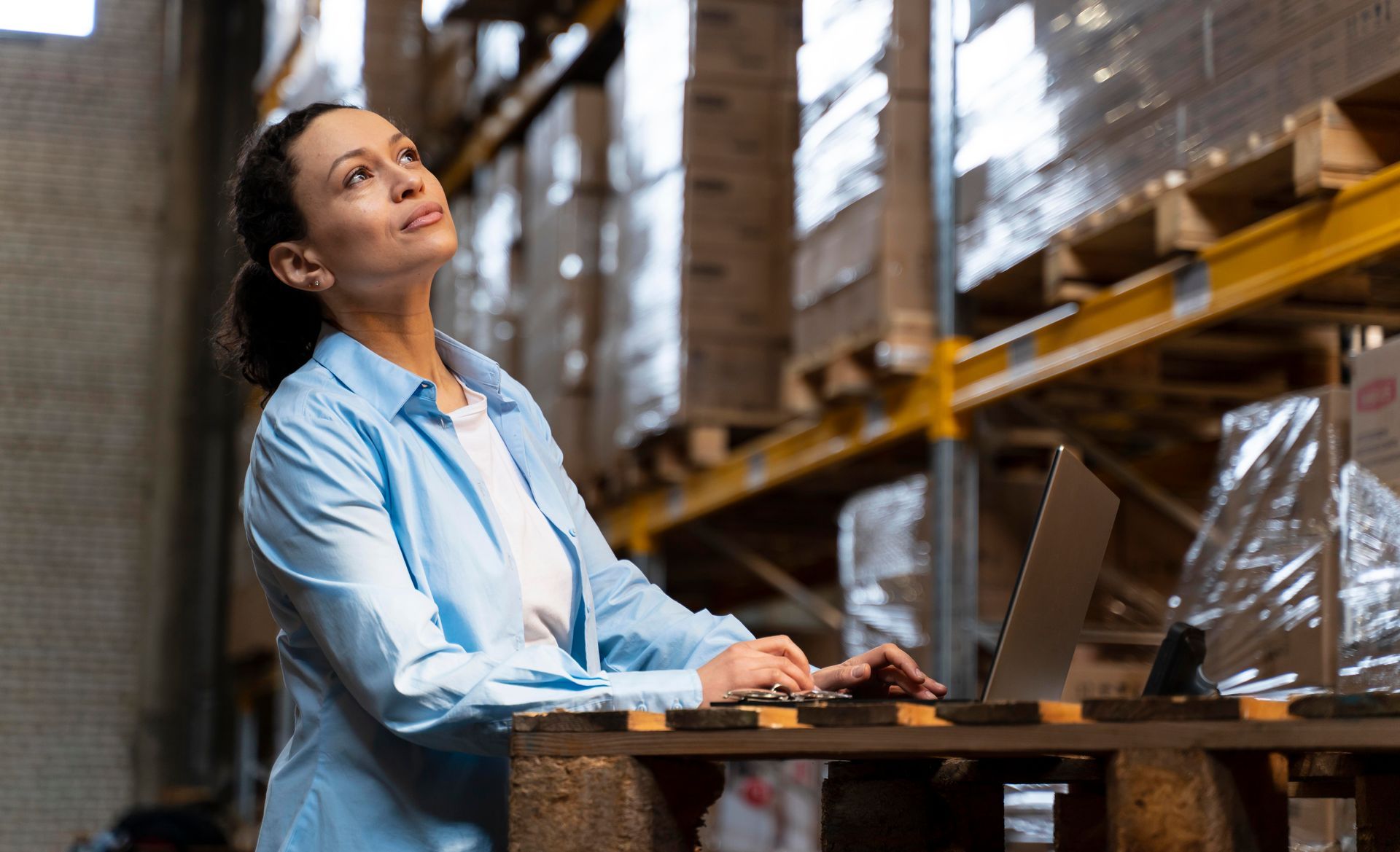Mulher analisando estoque com notebook em galpão de cosméticos e produtos armazenados
