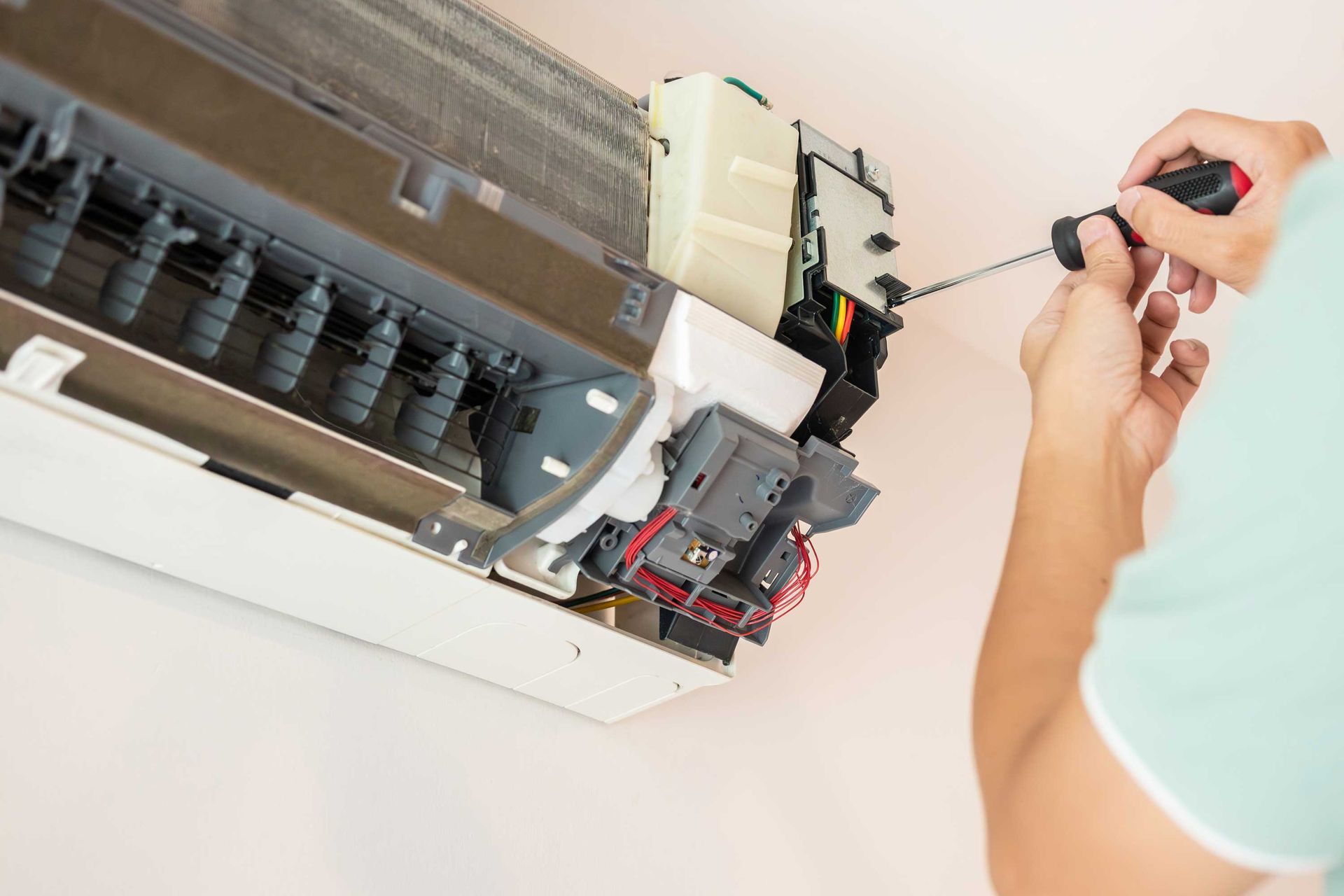 Technician using a screwdriver to repair the internal components of a wall-mounted AC unit. Technician using a screwdriver to repair the internal components of a wall-mounted AC unit.