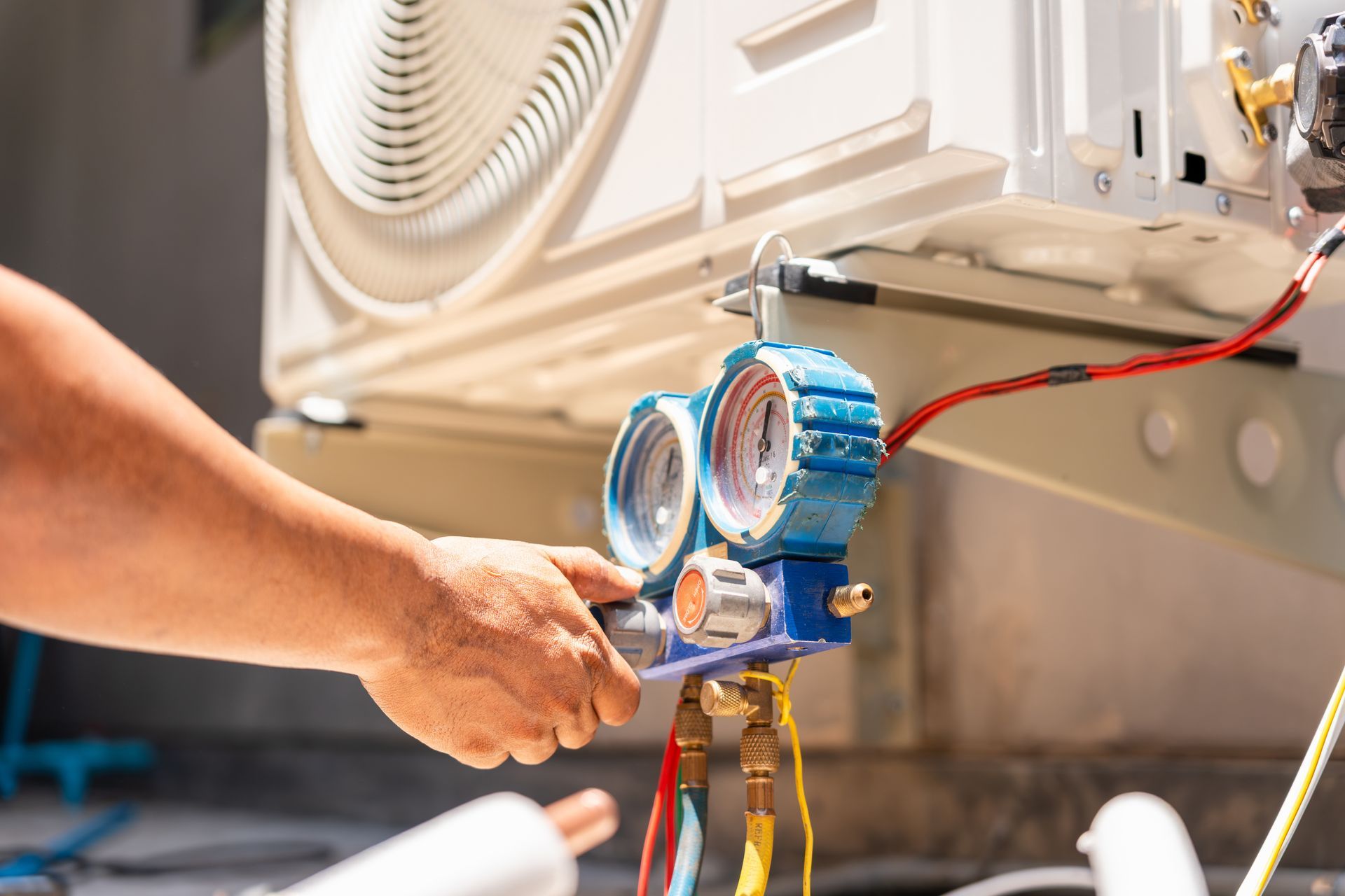 The hand of a technician using a manifold gauge to check an air conditioner refrigerant pressure.