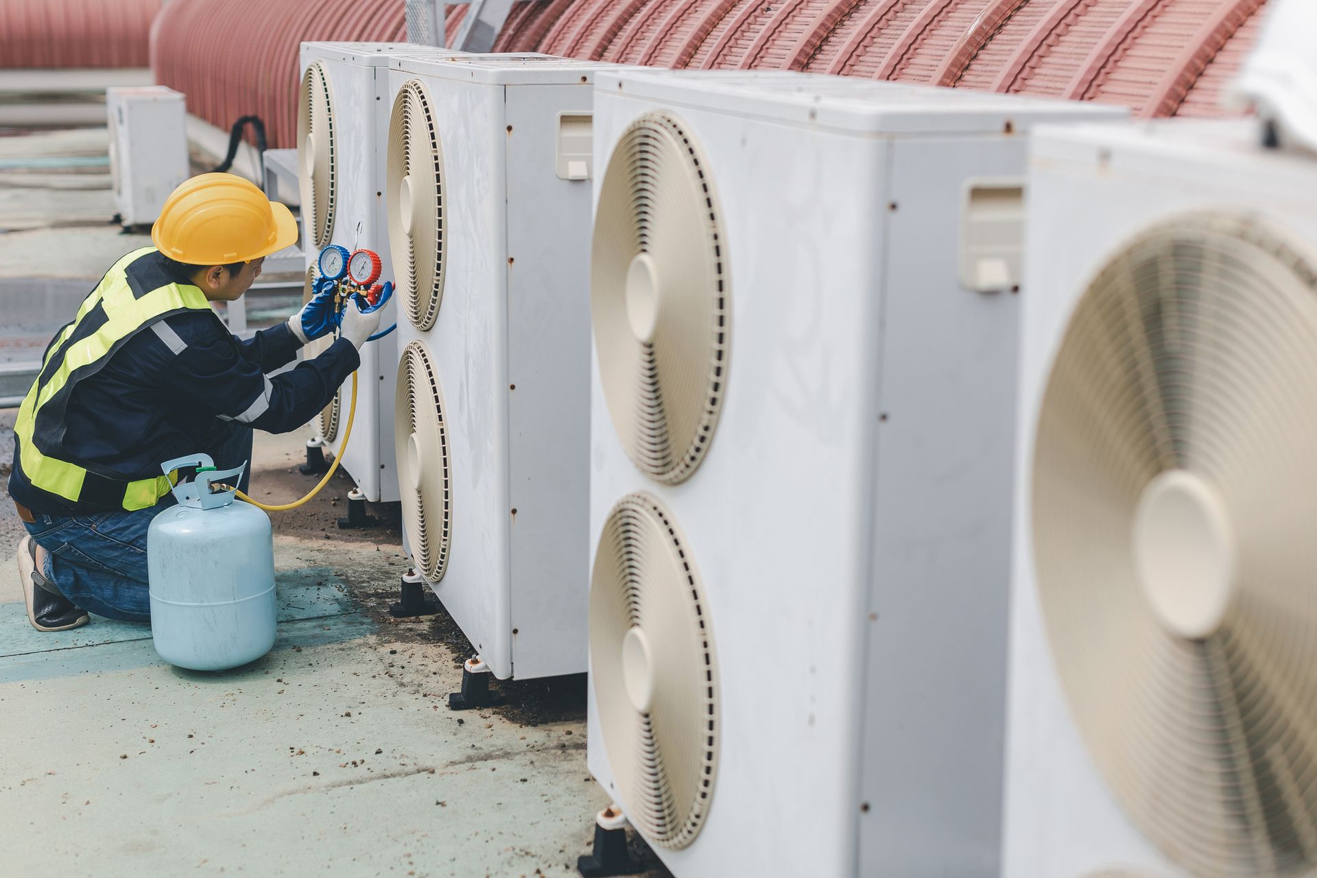 Commercial air conditioning repair technician checking HVAC system pressure with gauges.