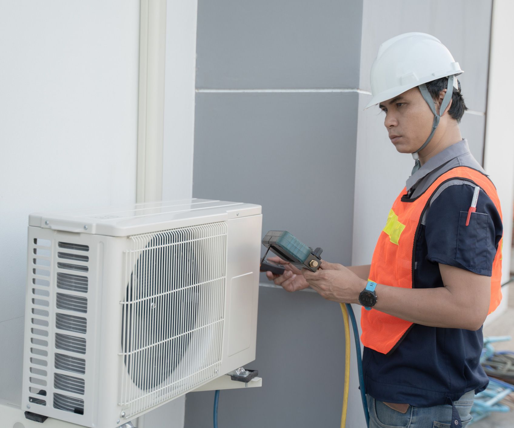 A male HVAC contractor checks on an outdoor unit, while wearing safety gear.