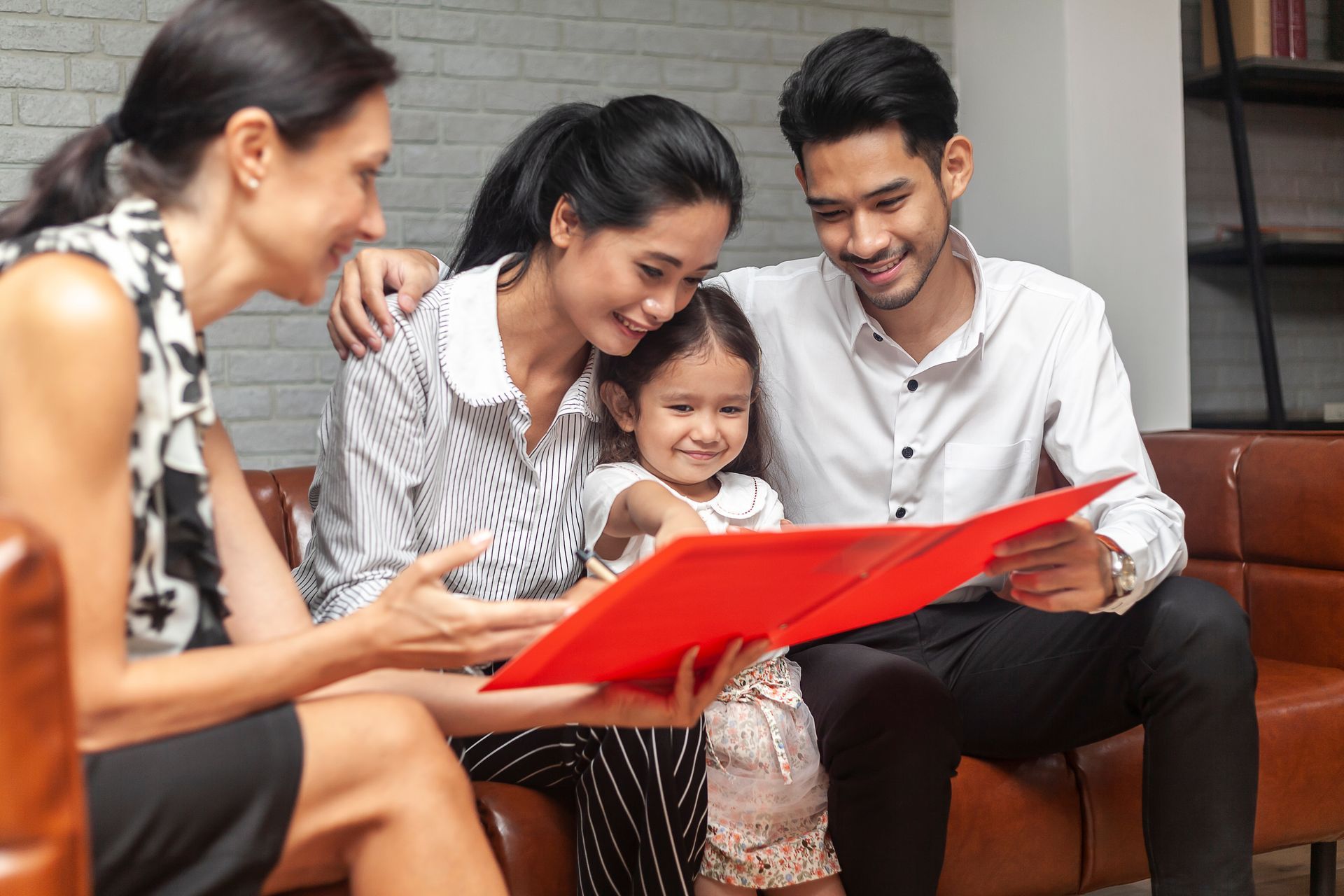 Family with child looking at a red book with an advisor; indoors, smiling.