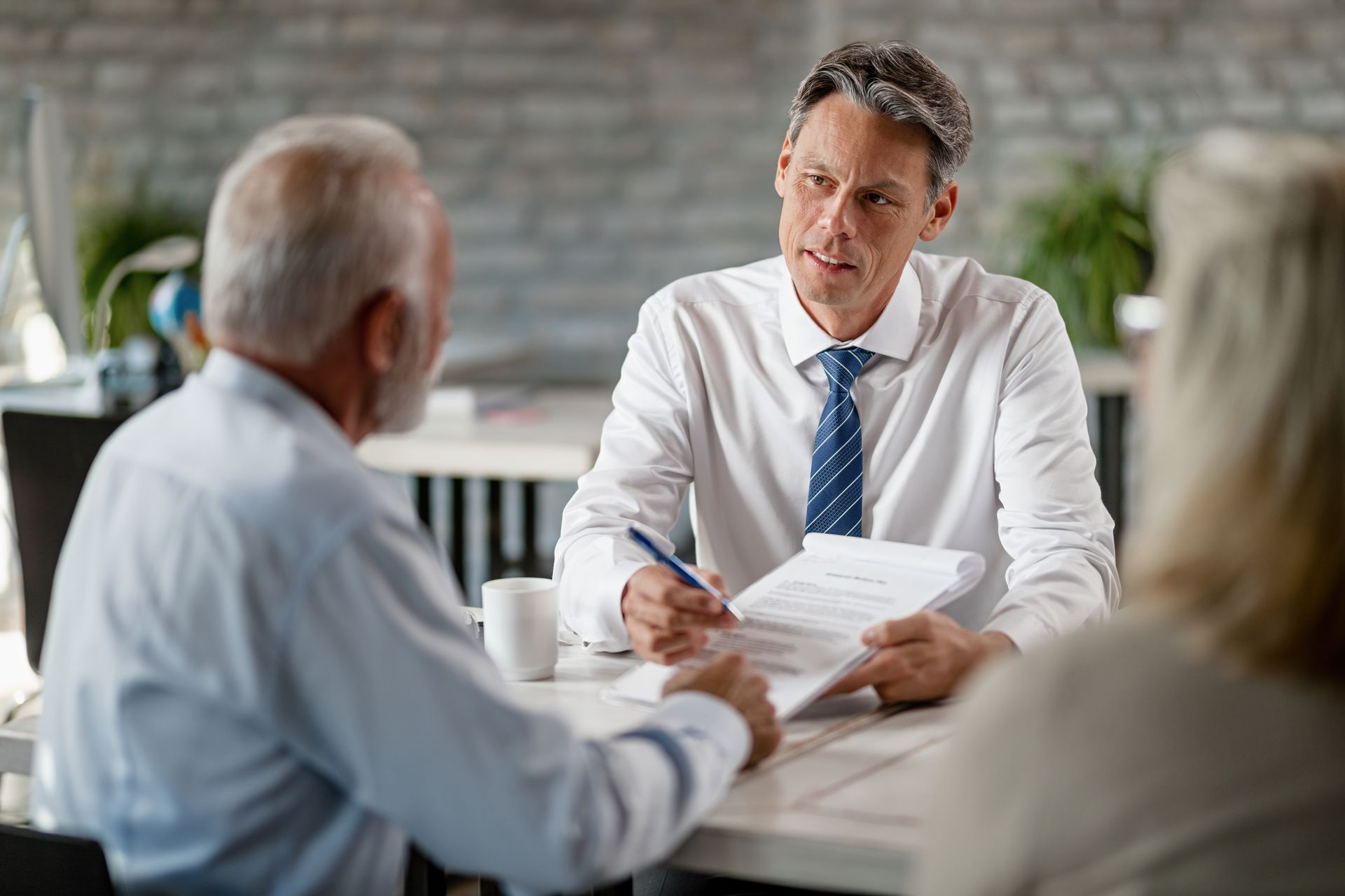 A financial advisor reviews documents with an older couple at a table in an office setting.