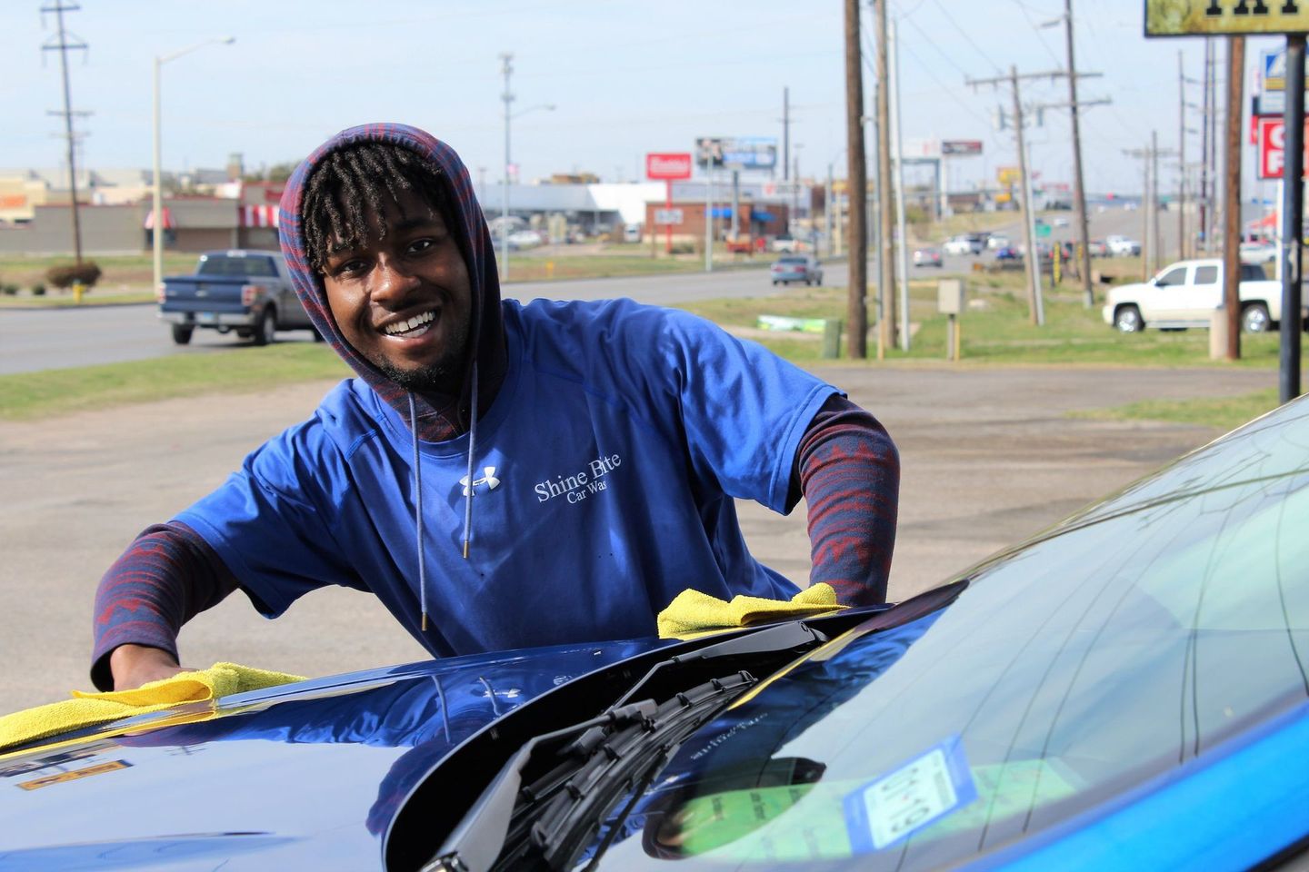 A man in a blue shirt is cleaning the windshield of a blue car.