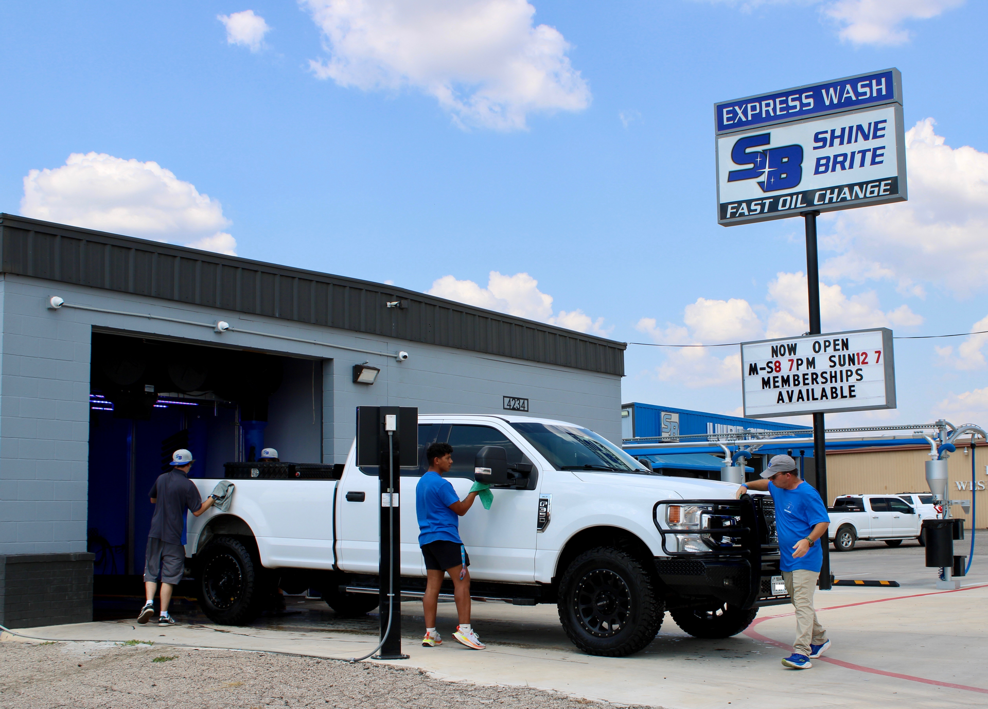 A white pickup truck being cleaned at an Express Wash. Workers are wiping down the vehicle under a blue sky.
