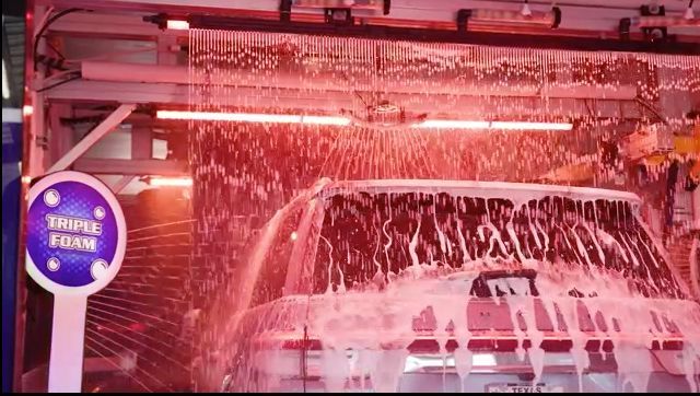 Car being washed with triple foam at a car wash. Red lighting.