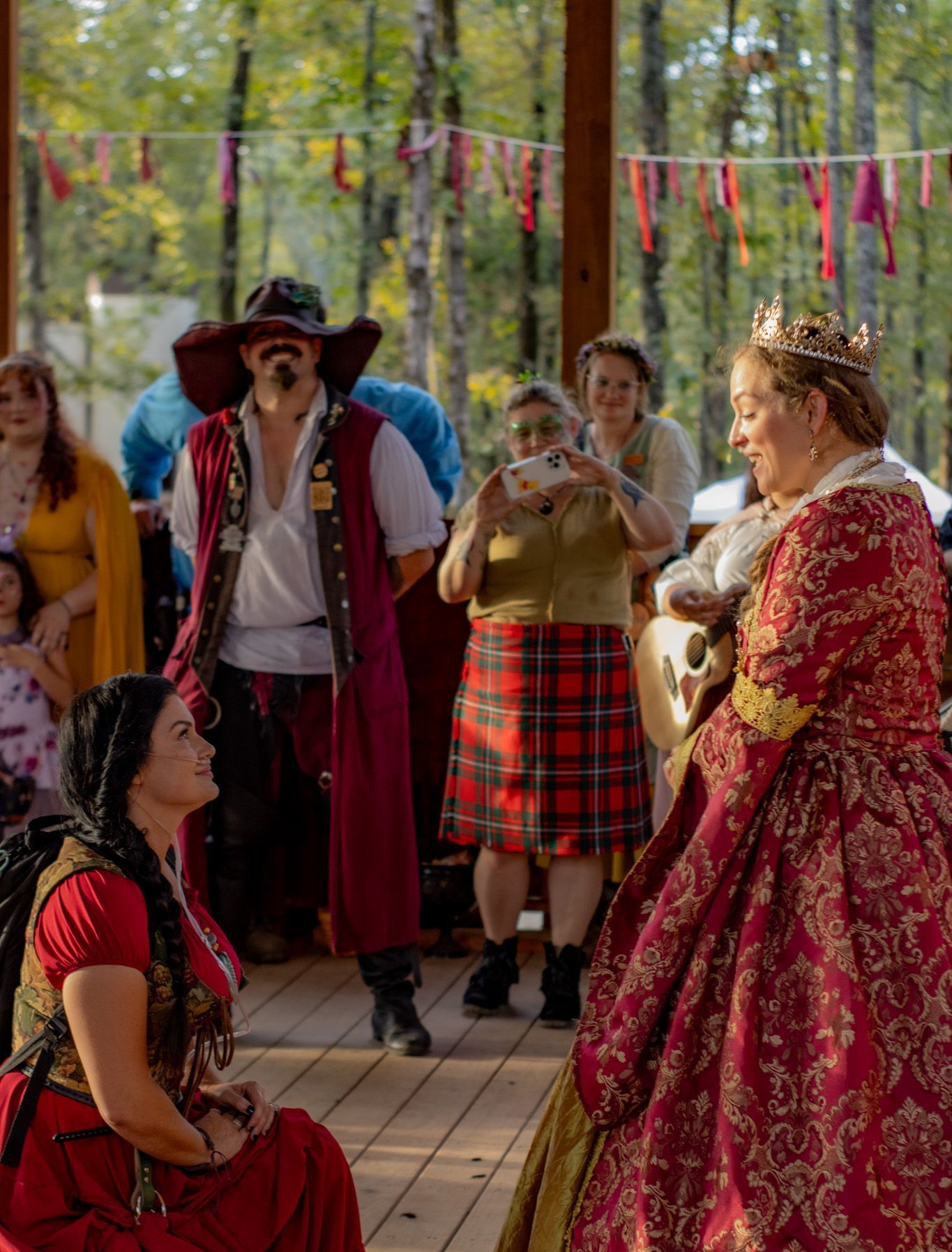 A group of people dressed in medieval costumes are standing around a woman in a red dress.