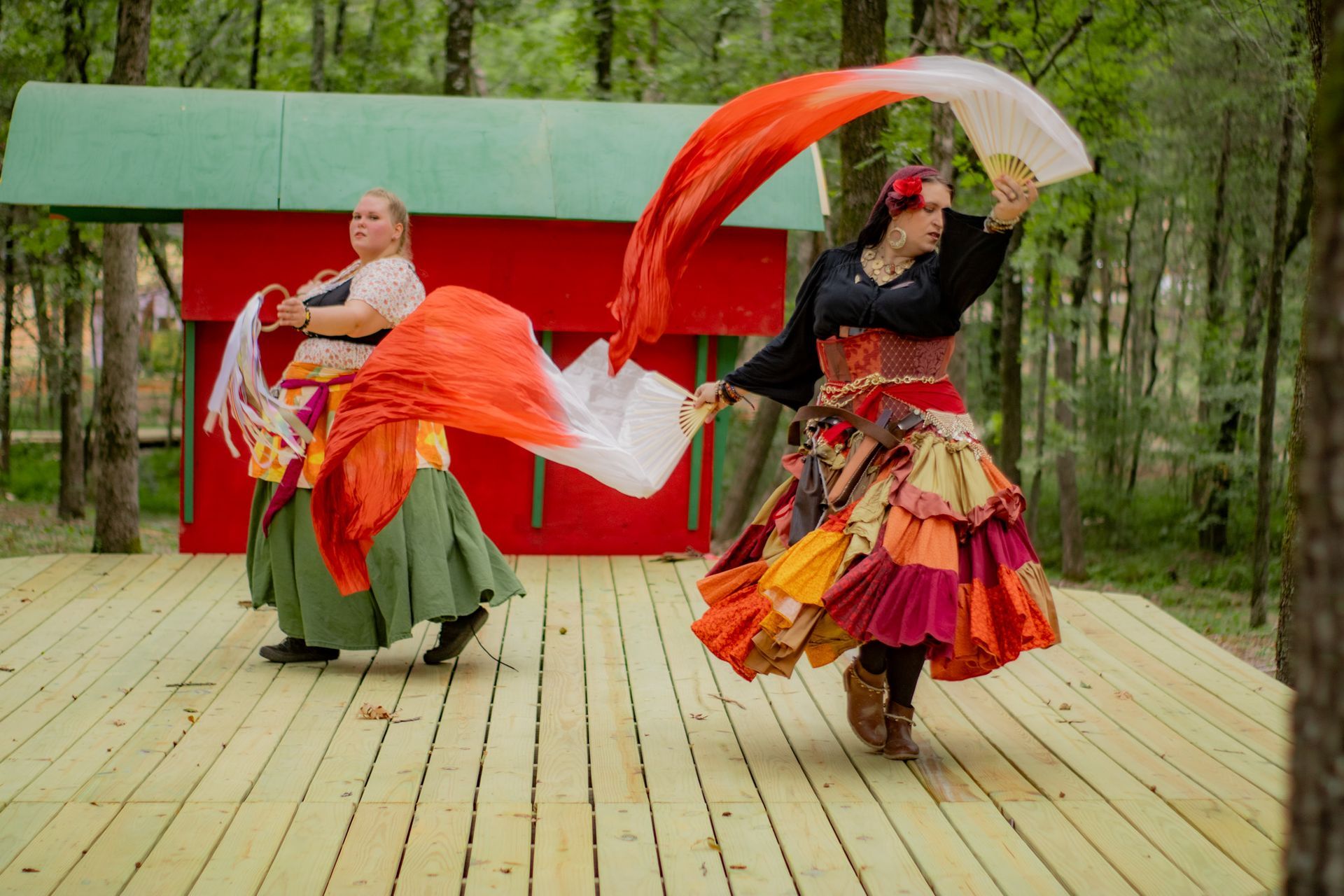 Two women in colorful skirts are dancing on a wooden stage.
