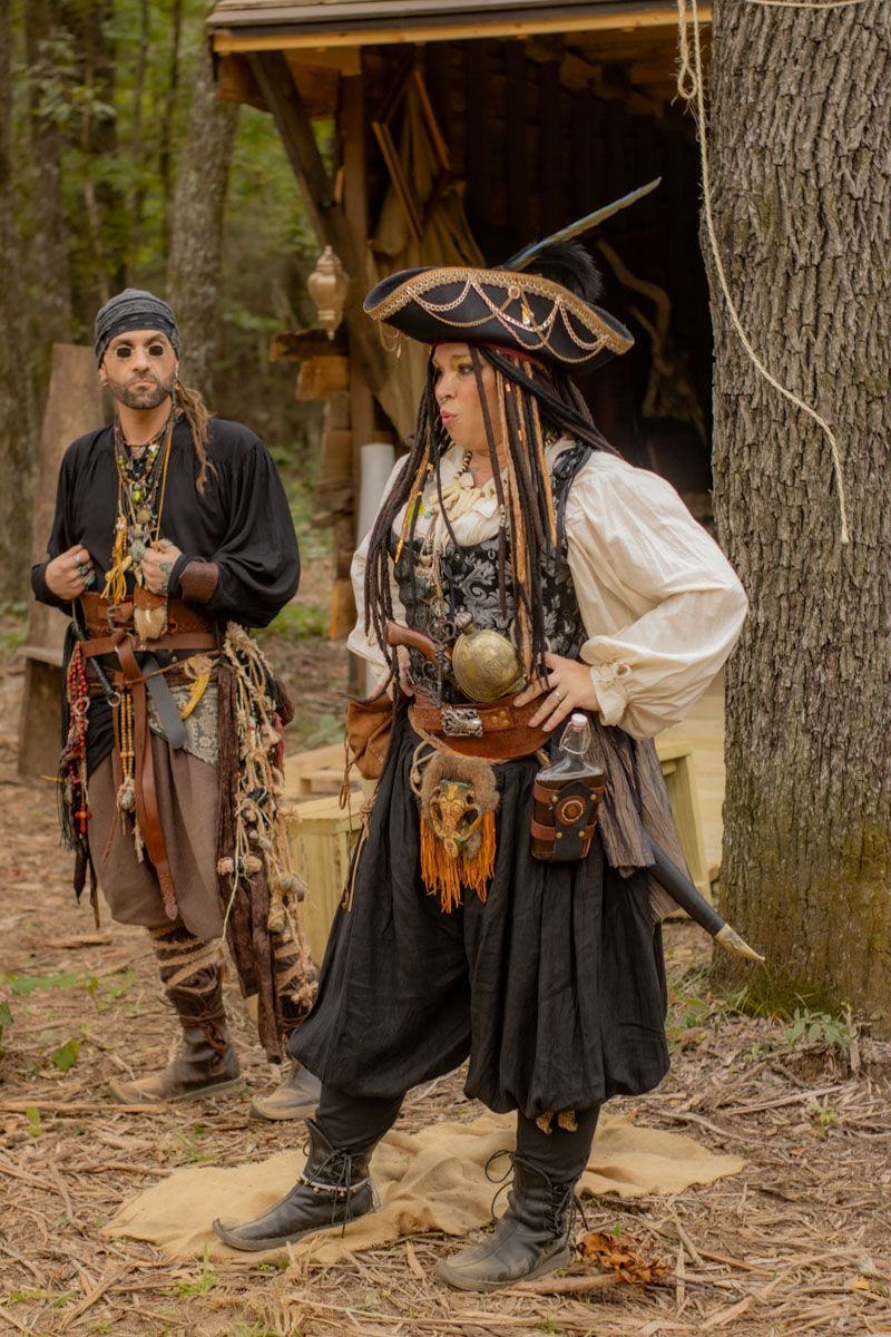 A man and a woman dressed as pirates are standing next to each other in the woods.