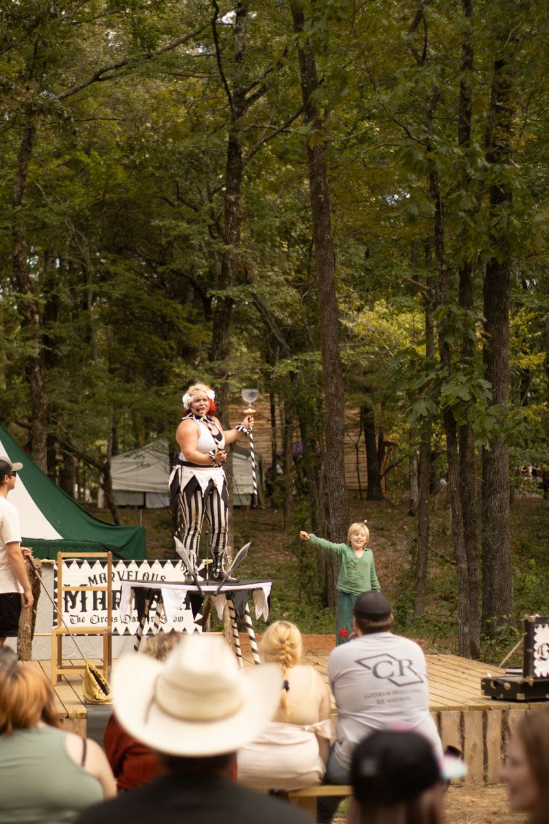 A group of people are sitting in the woods watching a performance.