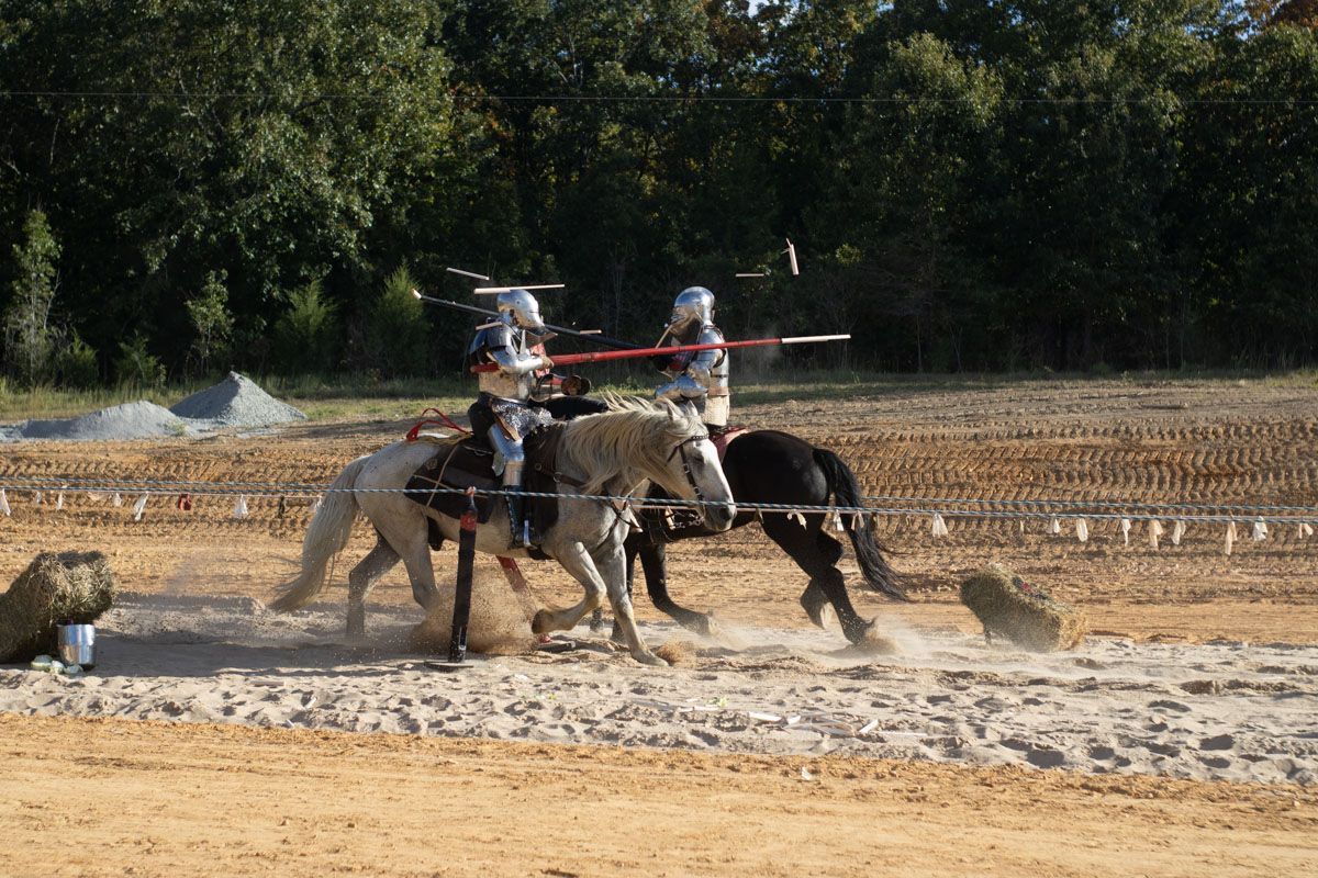 Two men are riding horses in a field while holding swords.