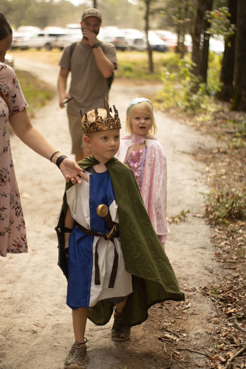 A woman is holding the hand of a little boy dressed as a king.
