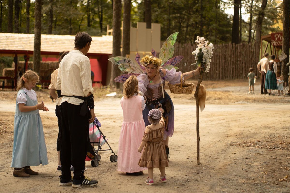 A woman dressed as a fairy is standing next to a group of children.