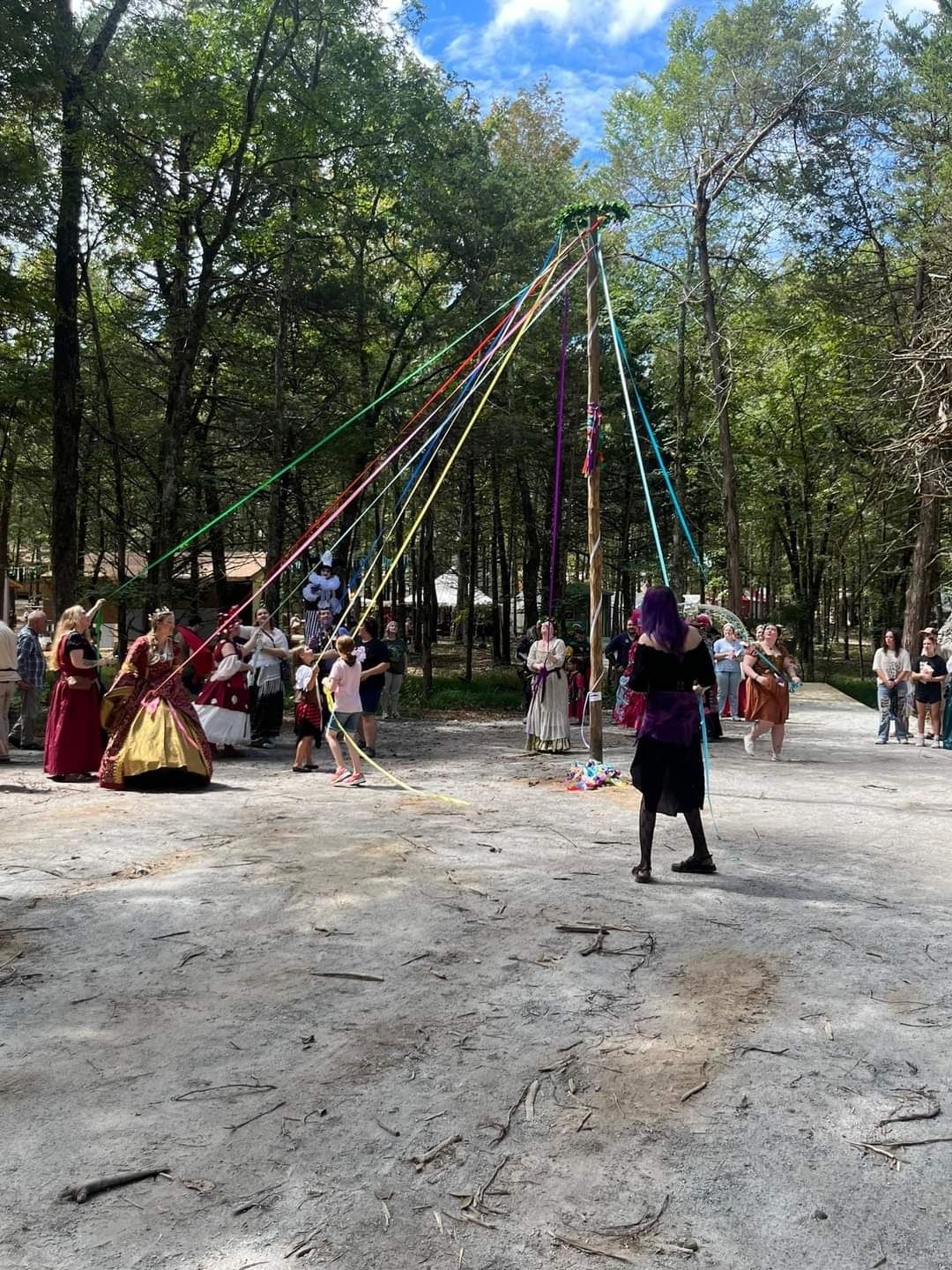 A group of people are dancing around a maypole in a park.