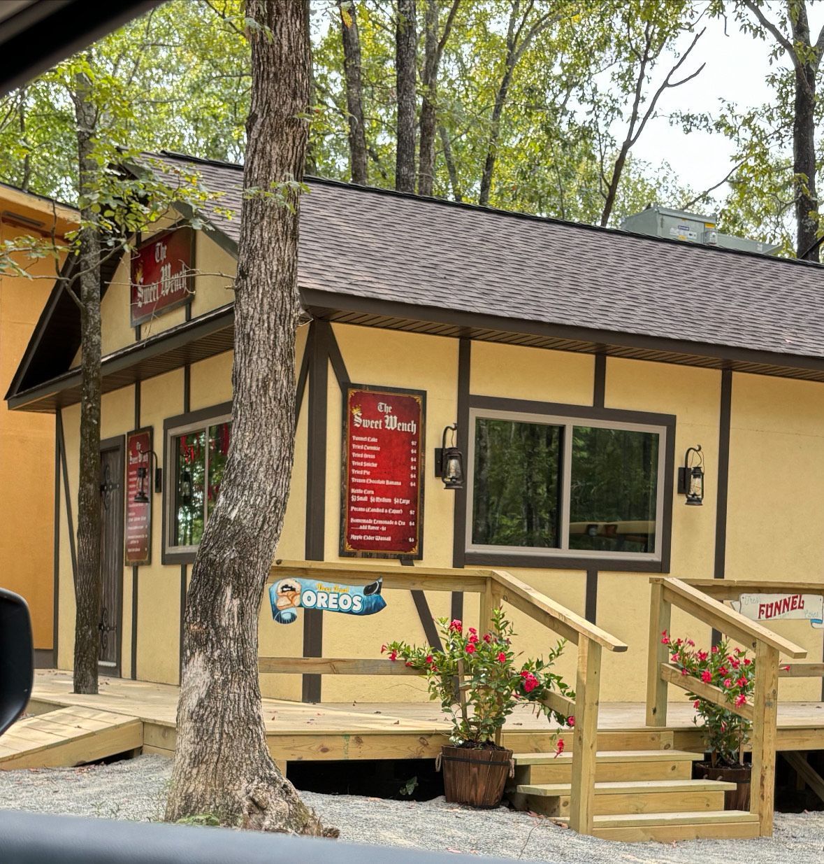 Small cottage-style business with a sign, windows, and a wooden deck. Trees surround the building.