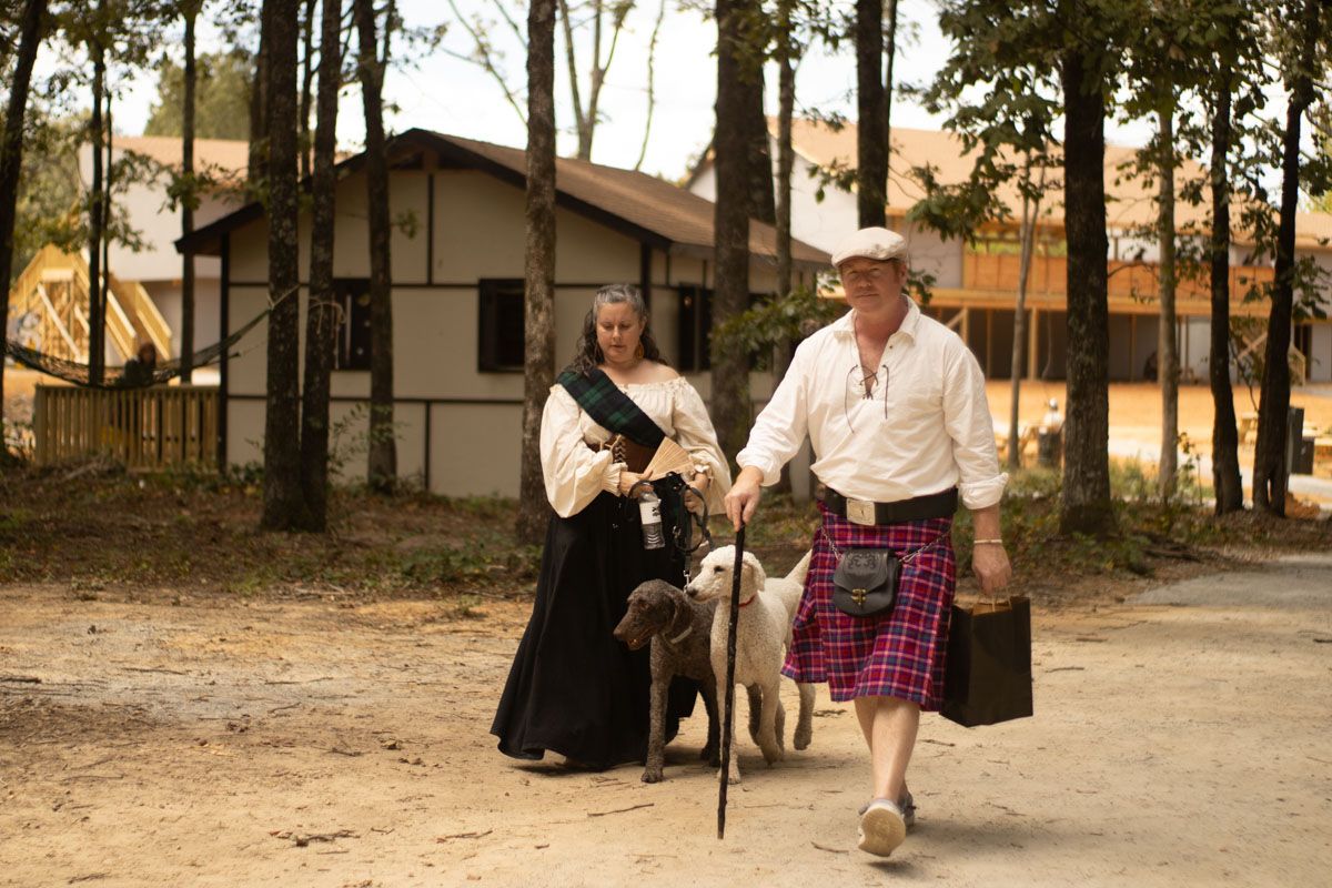 A man in a kilt is walking with a woman and a dog.