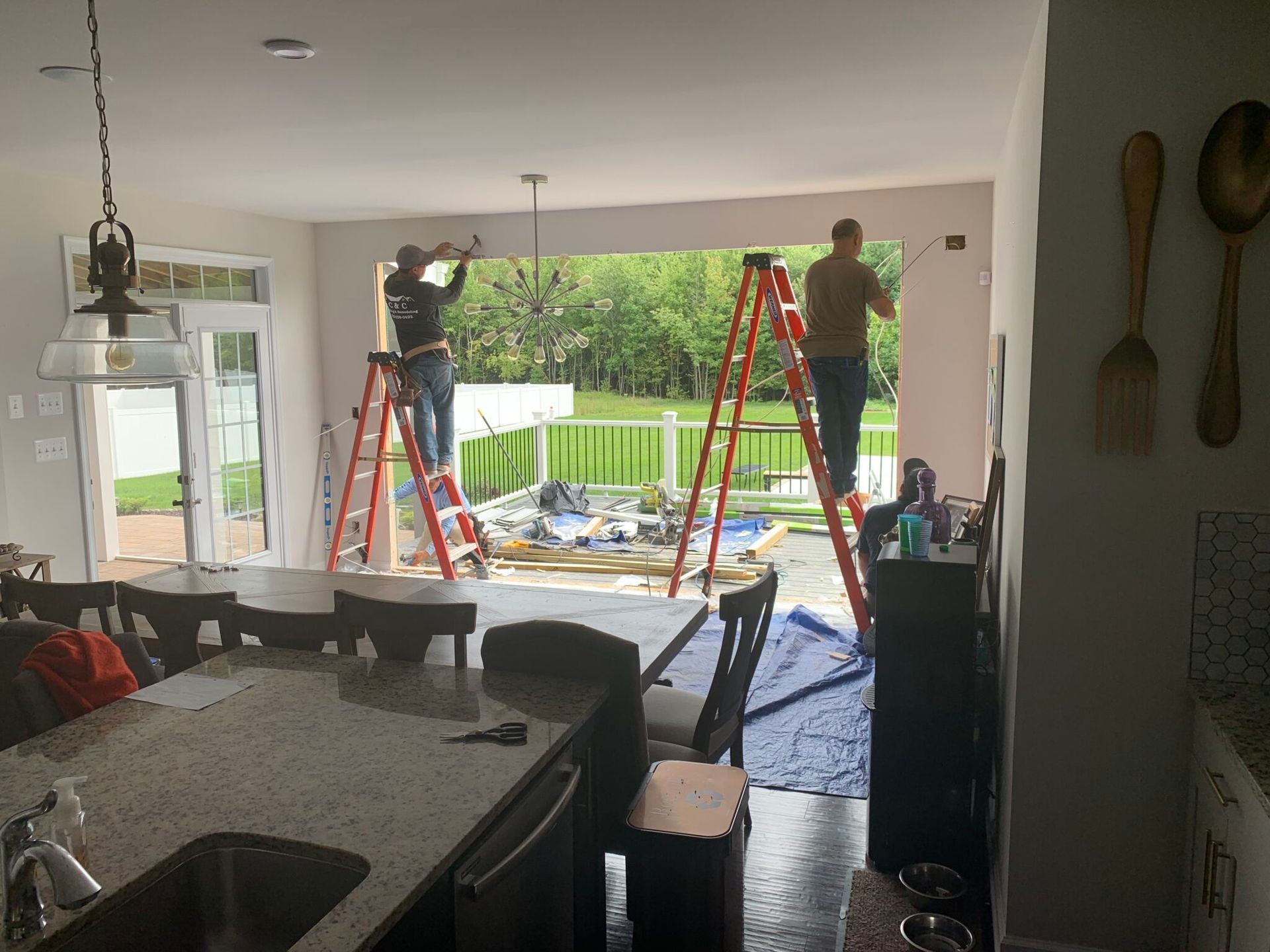 Two men are working on a sliding glass door in a kitchen.