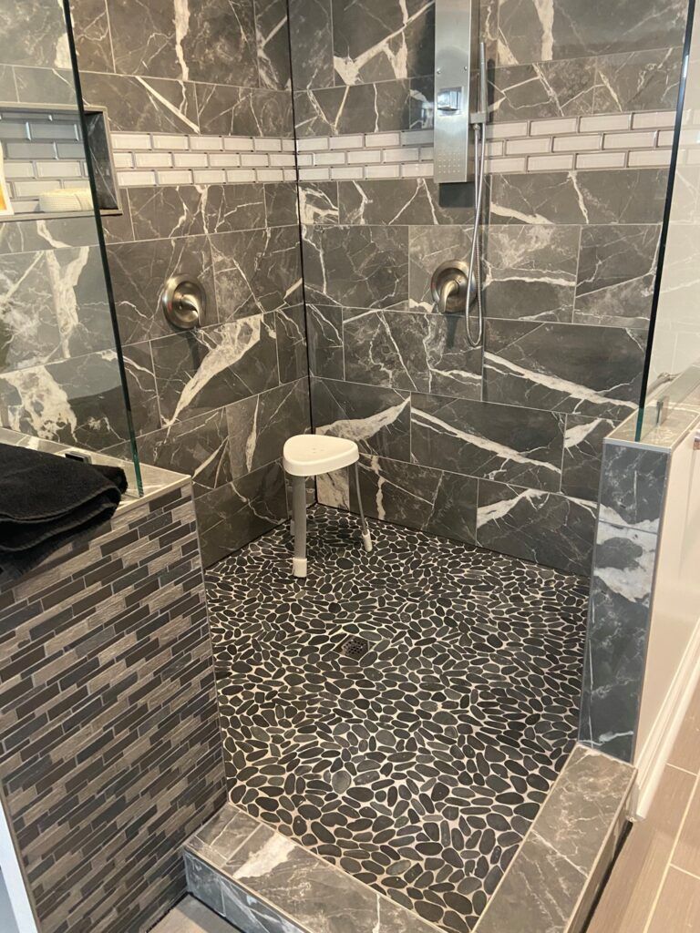 A walk in shower with a glass door and a stool.