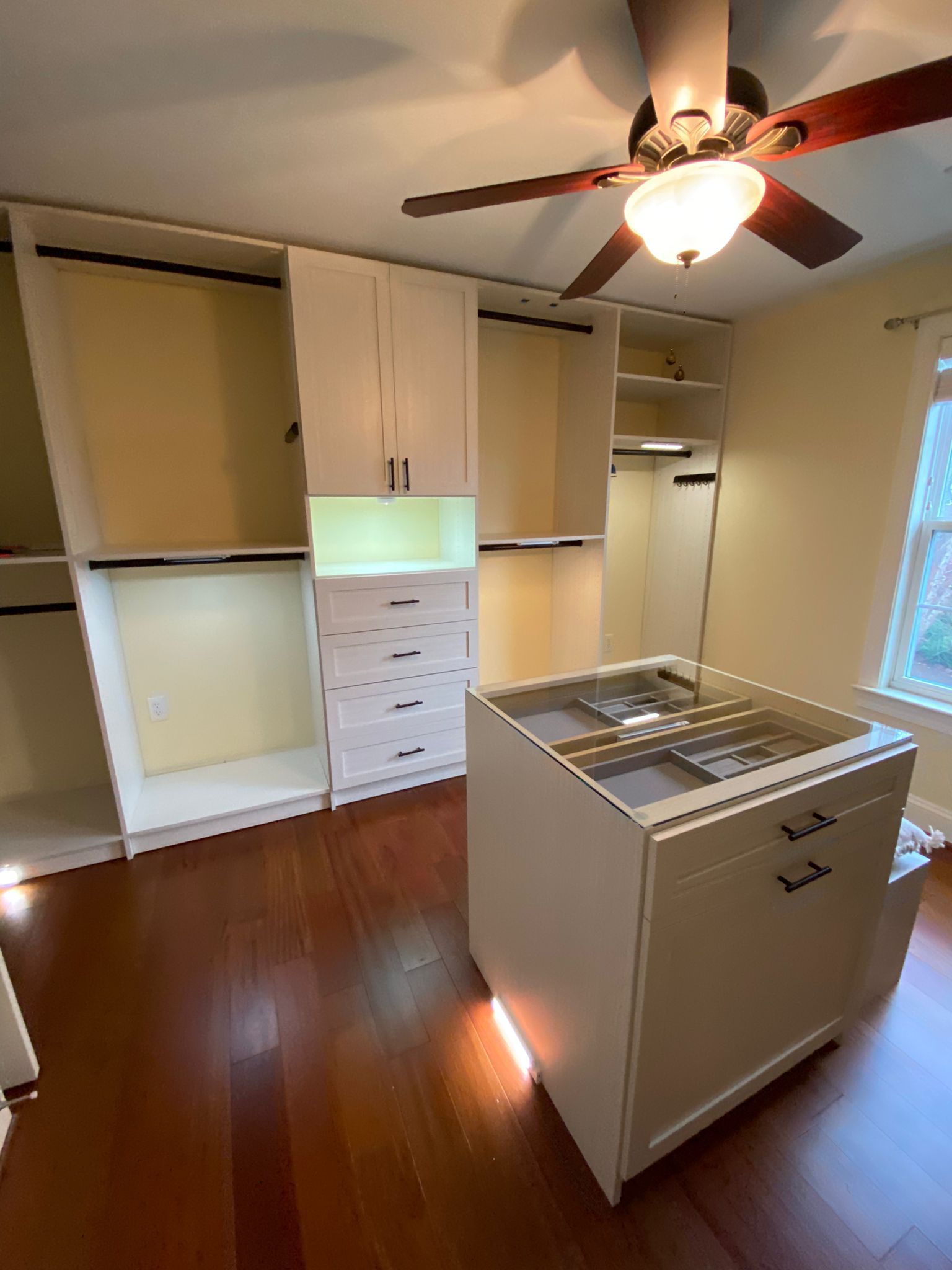 A walk in closet with a large island in the middle and a ceiling fan.