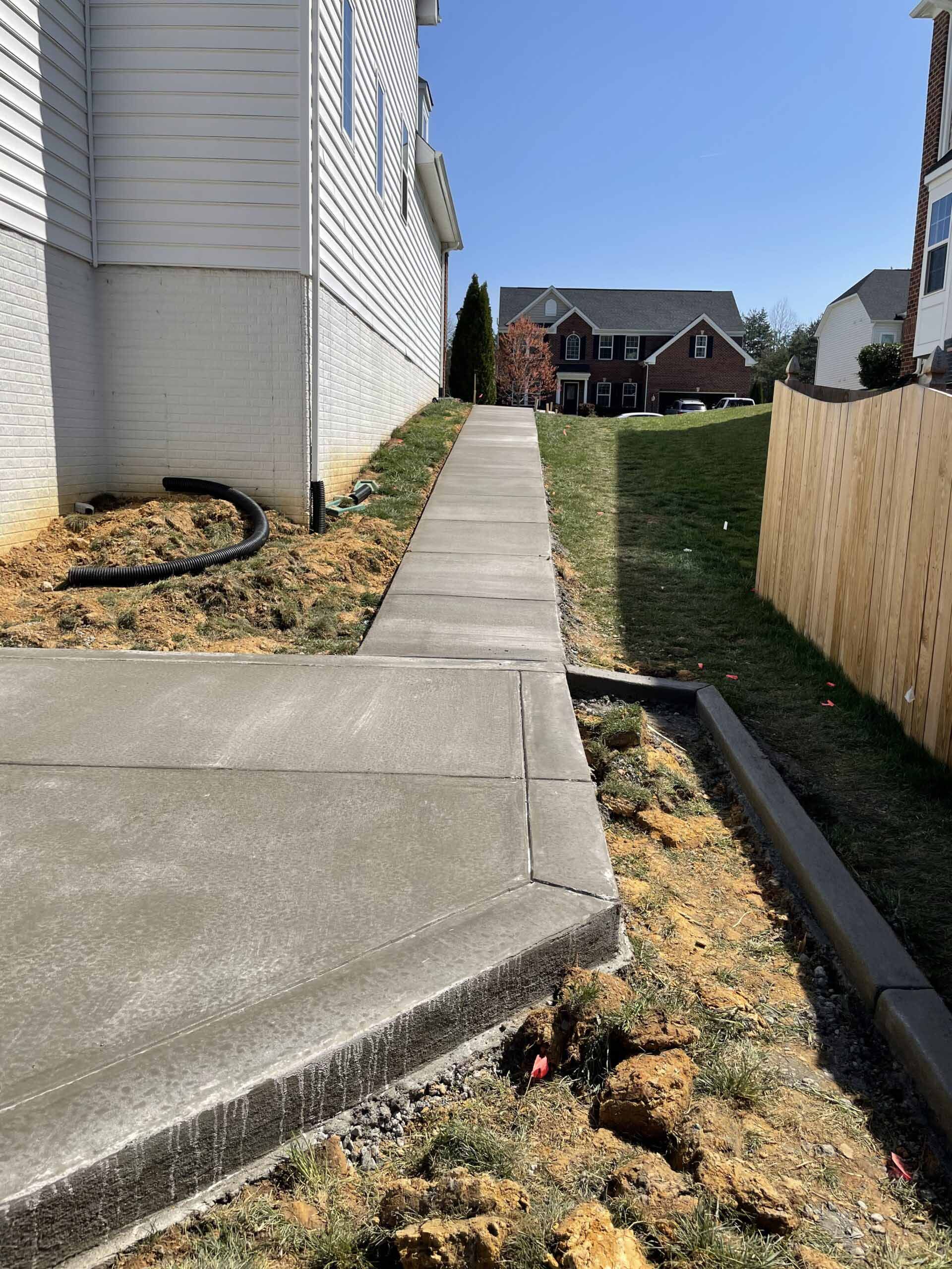 A concrete walkway leading to a house with a wooden fence.