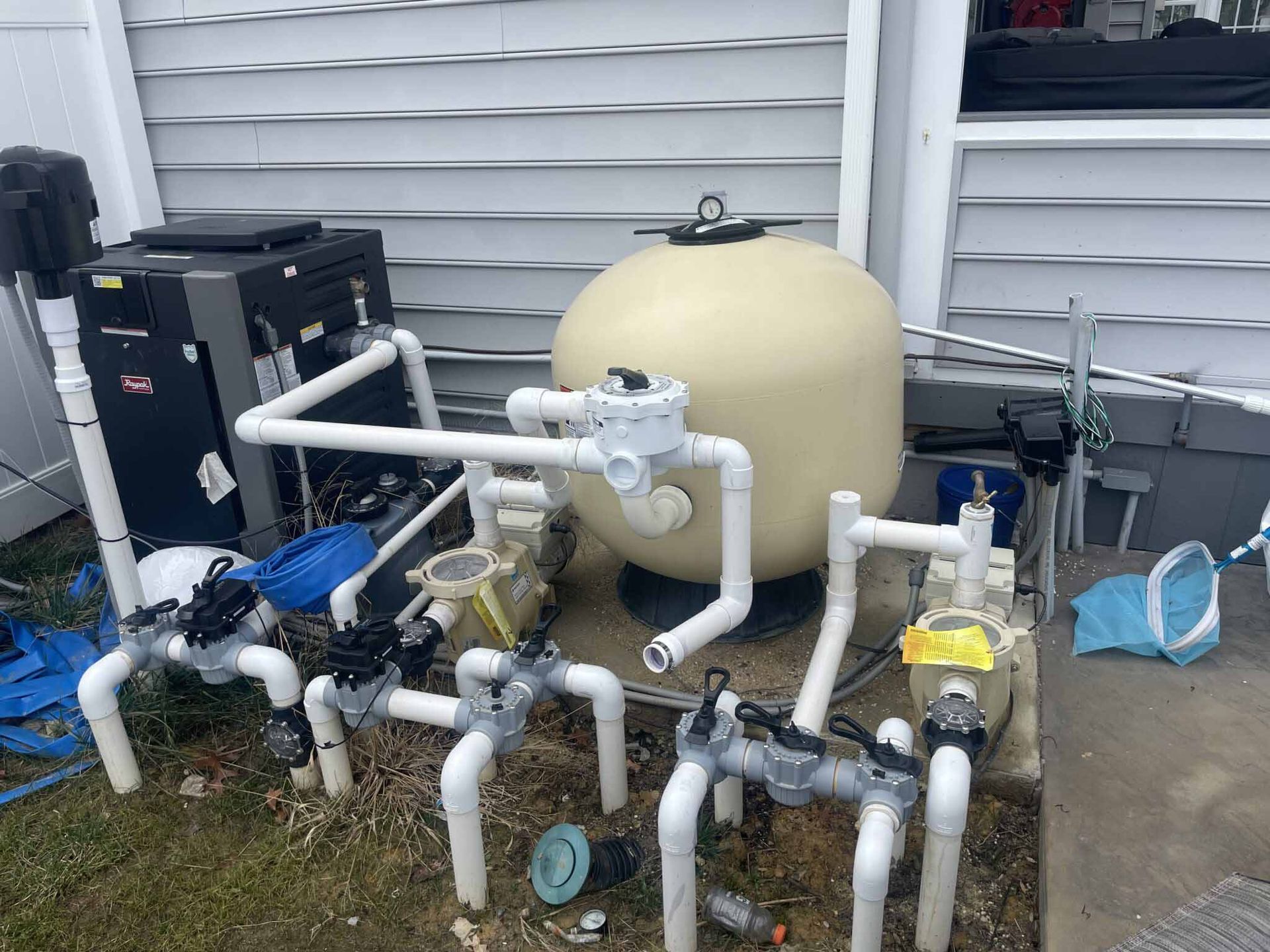 A swimming pool filter is sitting next to a bunch of pipes outside of a house.