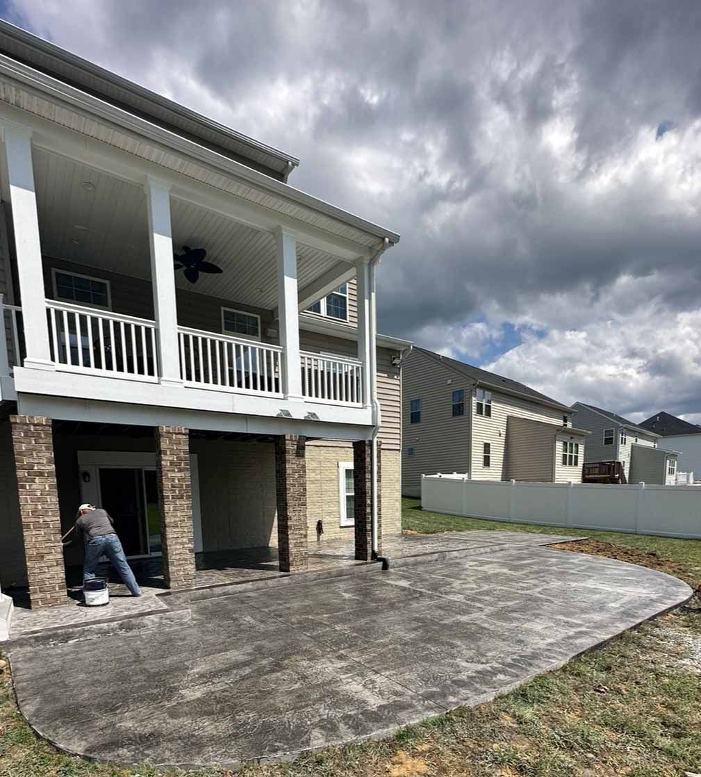 A man is working on a concrete patio in front of a house.
