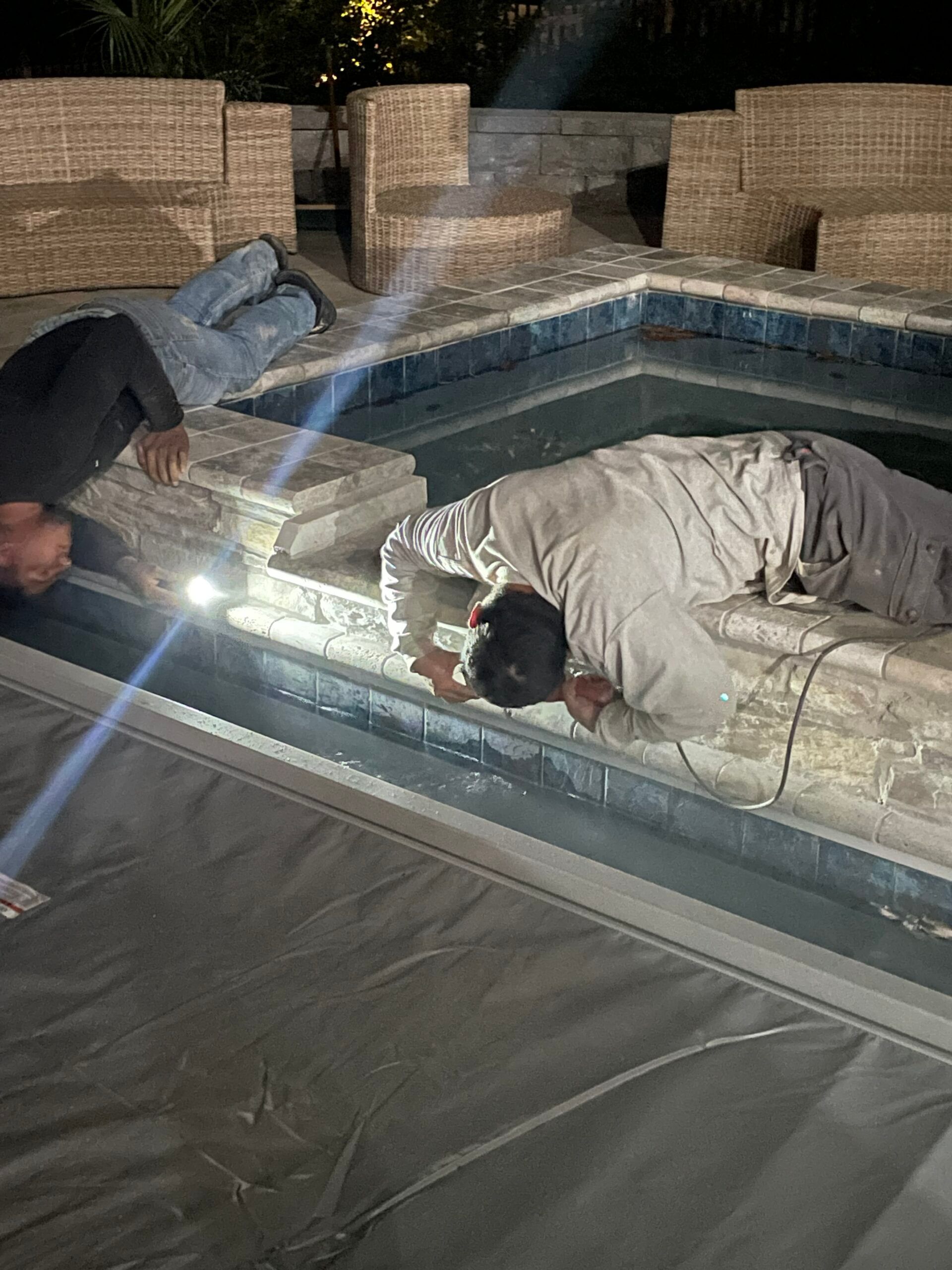 Two men are working on a swimming pool at night.