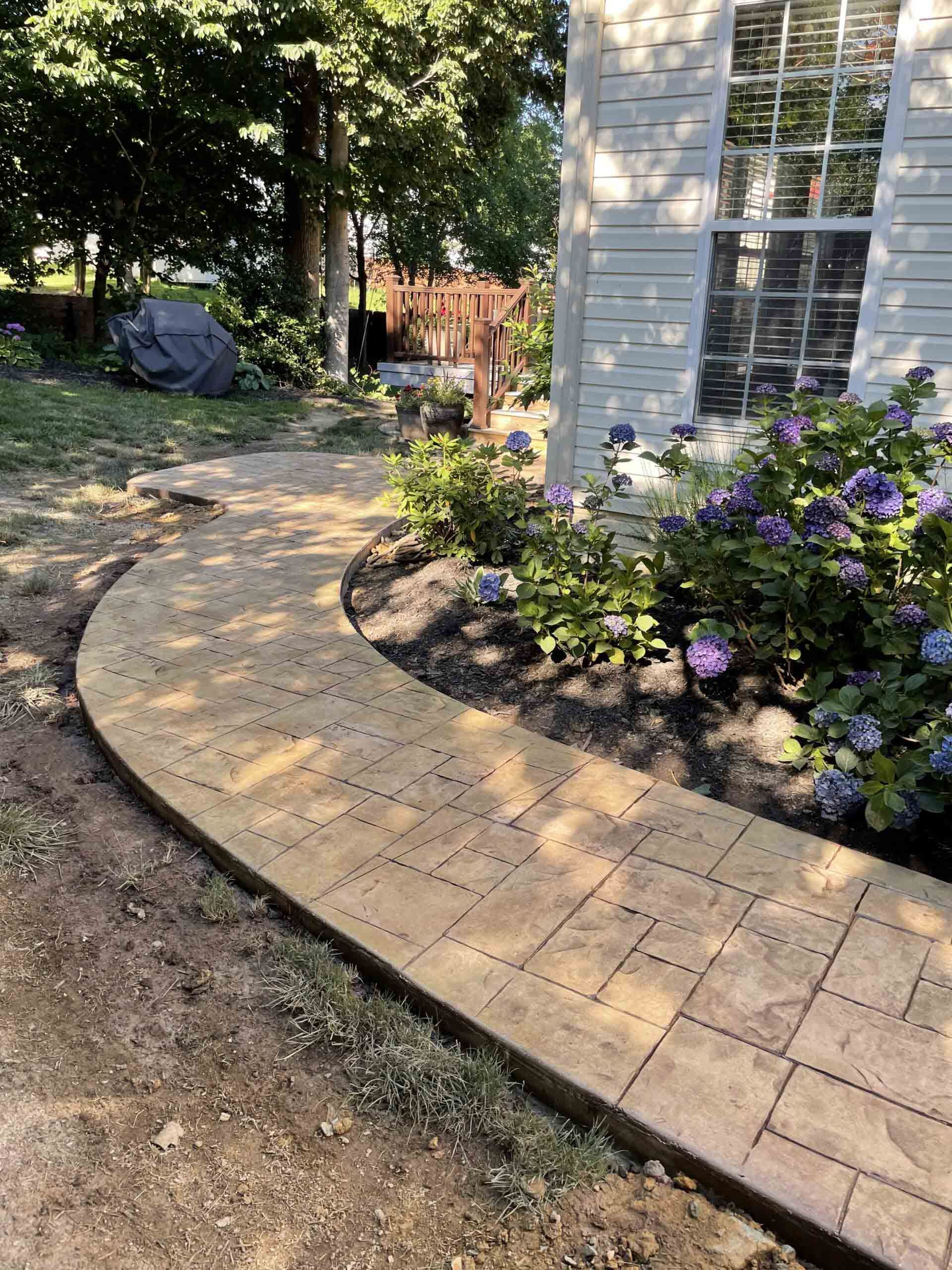 A curved walkway leading to a house with flowers in the background.