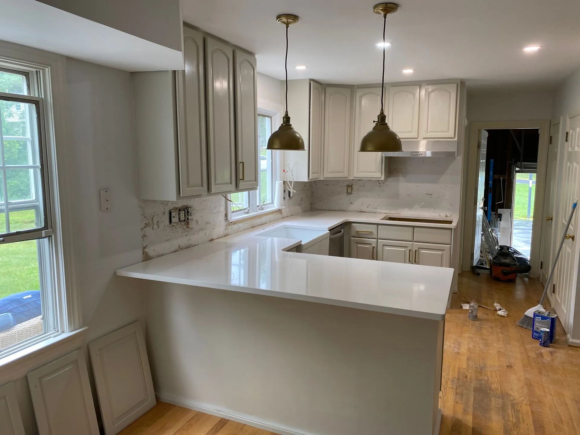 Kitchen renovation in progress, featuring white cabinets, quartz countertop, and gold pendant lights.