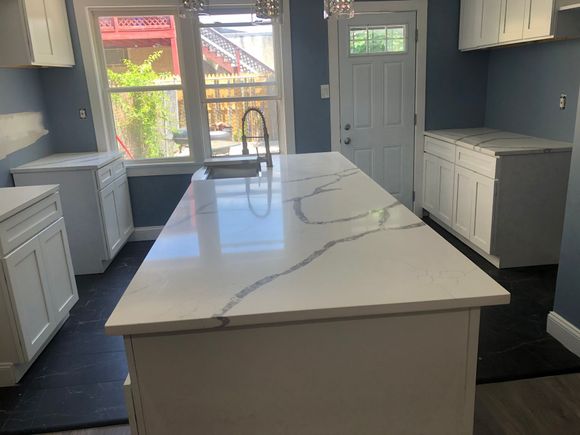 A kitchen with stainless steel appliances , wooden cabinets , white counter tops and a large island.