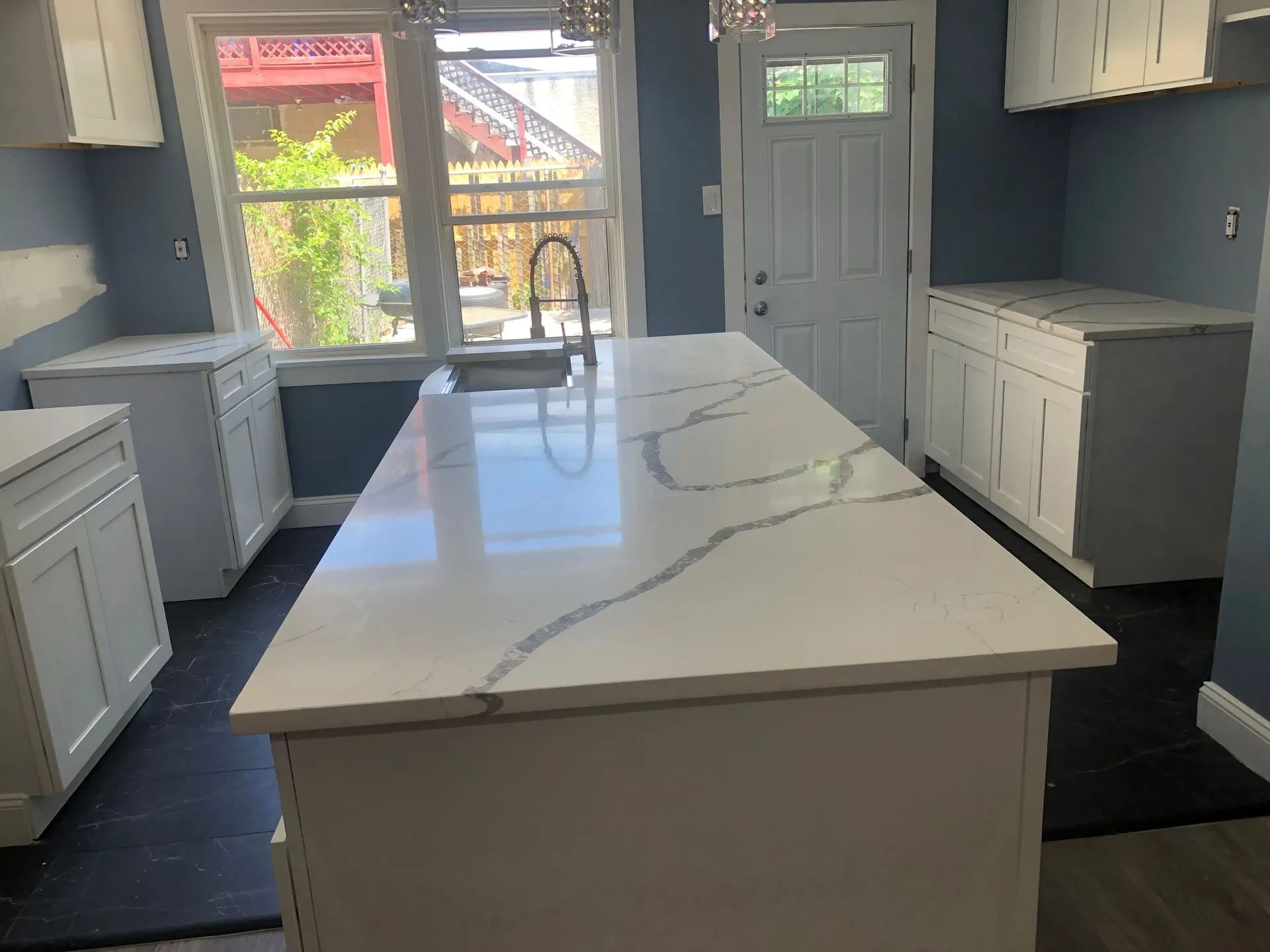 Kitchen with white cabinets, a large island, quartz countertop, and blue walls.