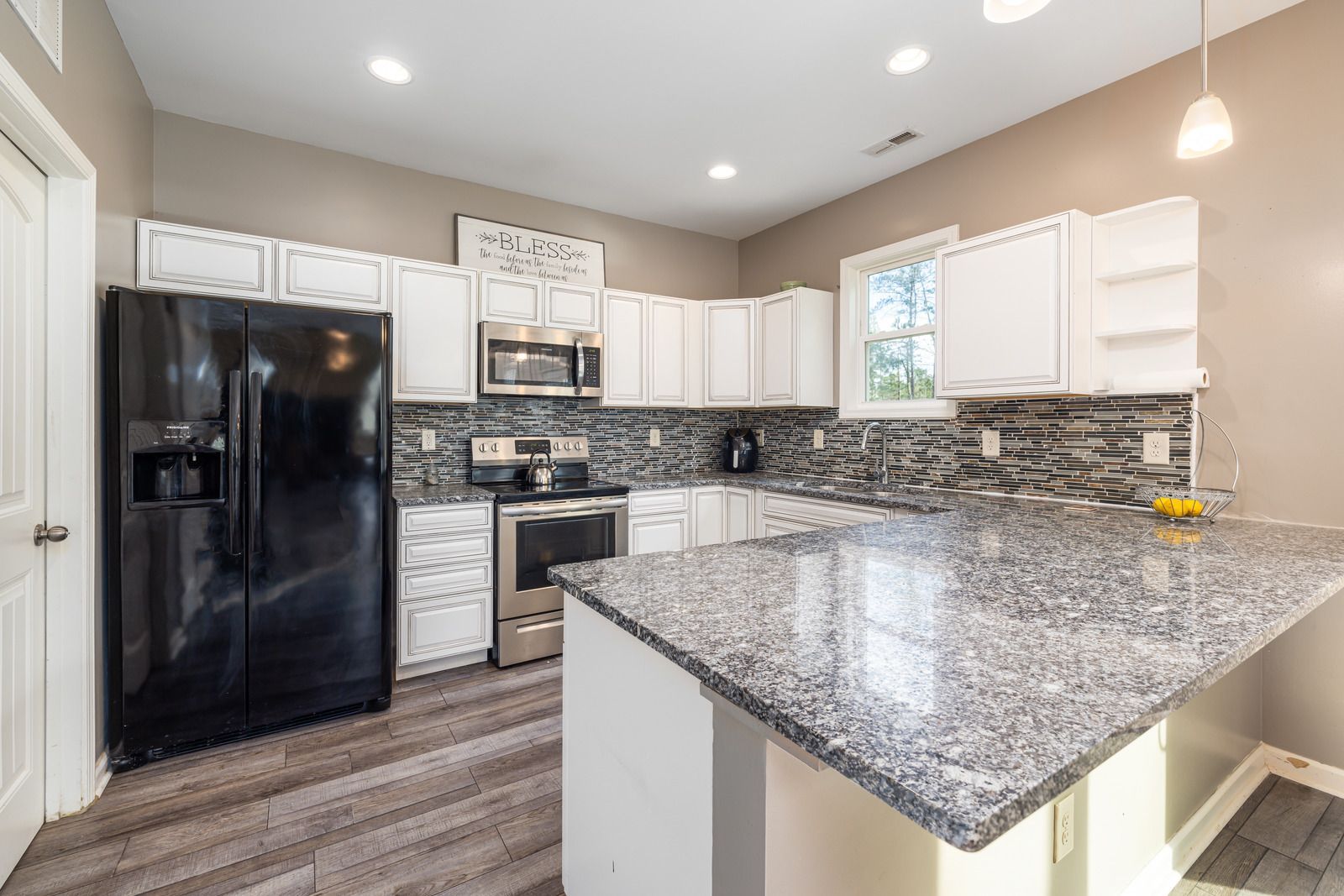 White kitchen with black appliances, gray countertop, and gray wood-look flooring.