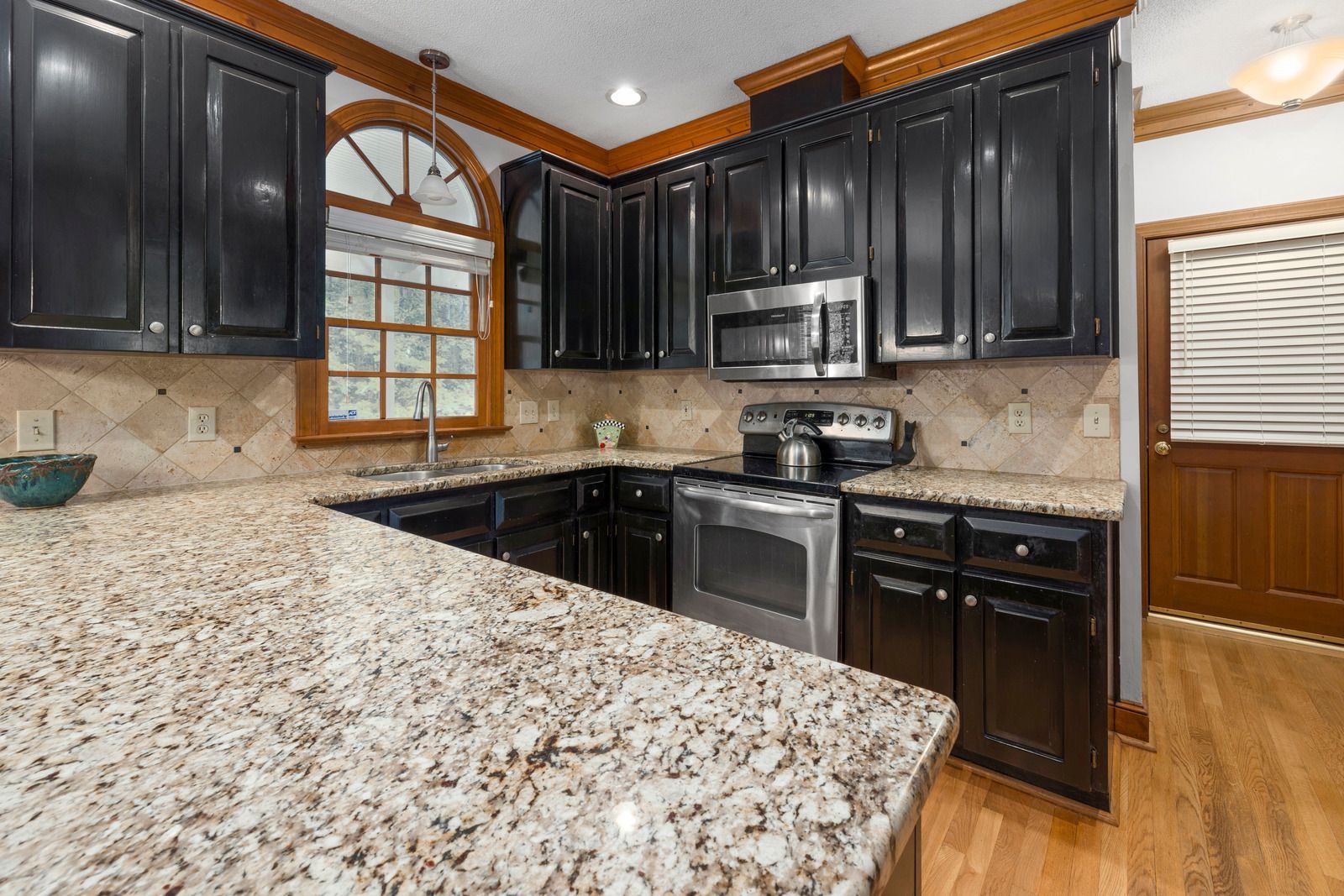 A kitchen with granite counter tops , black cabinets and stainless steel appliances.