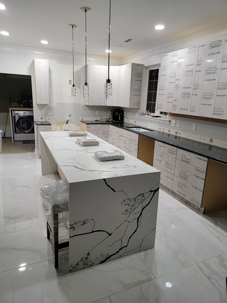 Newly renovated kitchen with white cabinets and countertops, black veining, and pendant lights.
