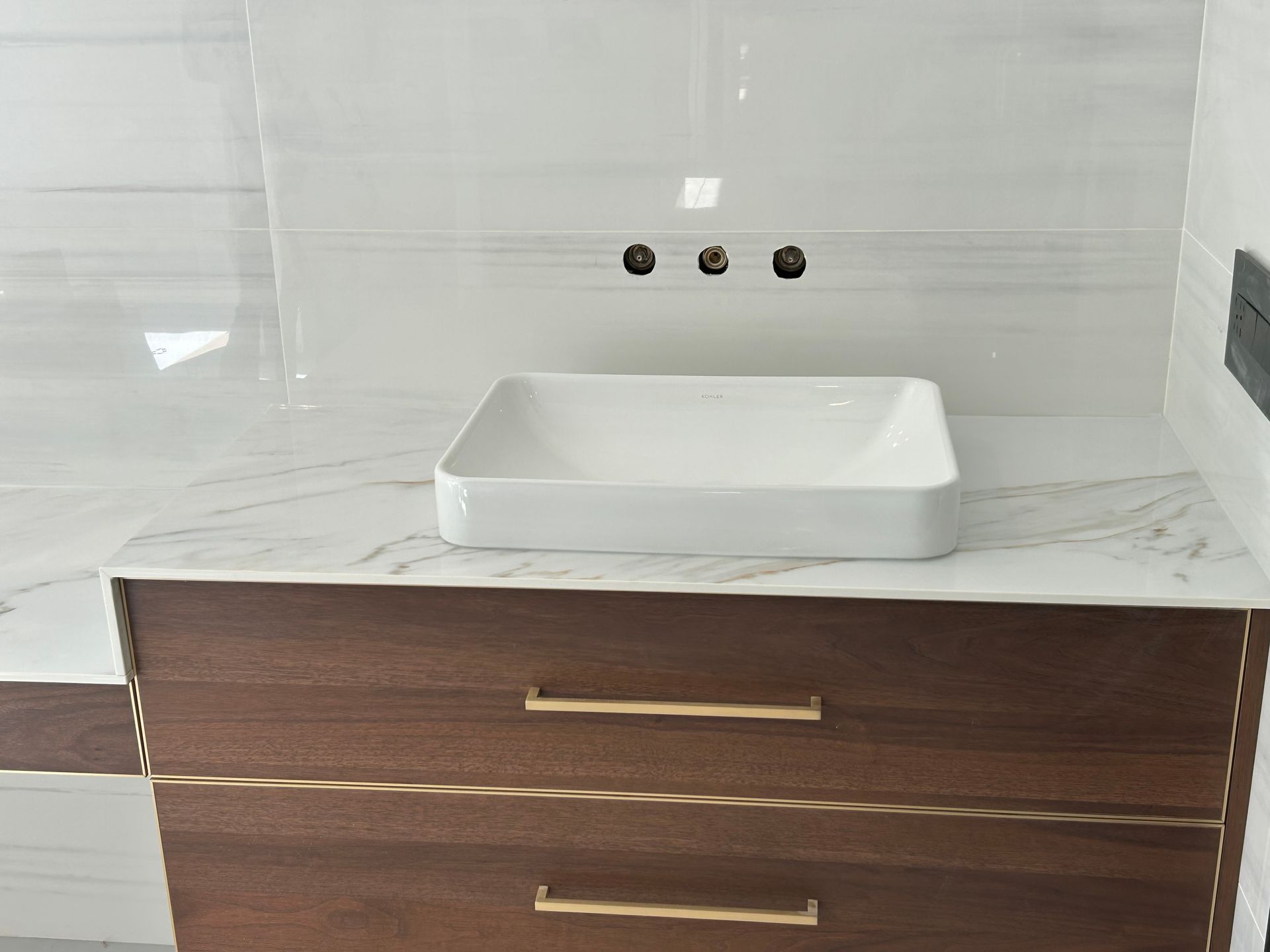 Bathroom vanity with white countertop, square sink, brown drawers, and wall-mounted faucet.