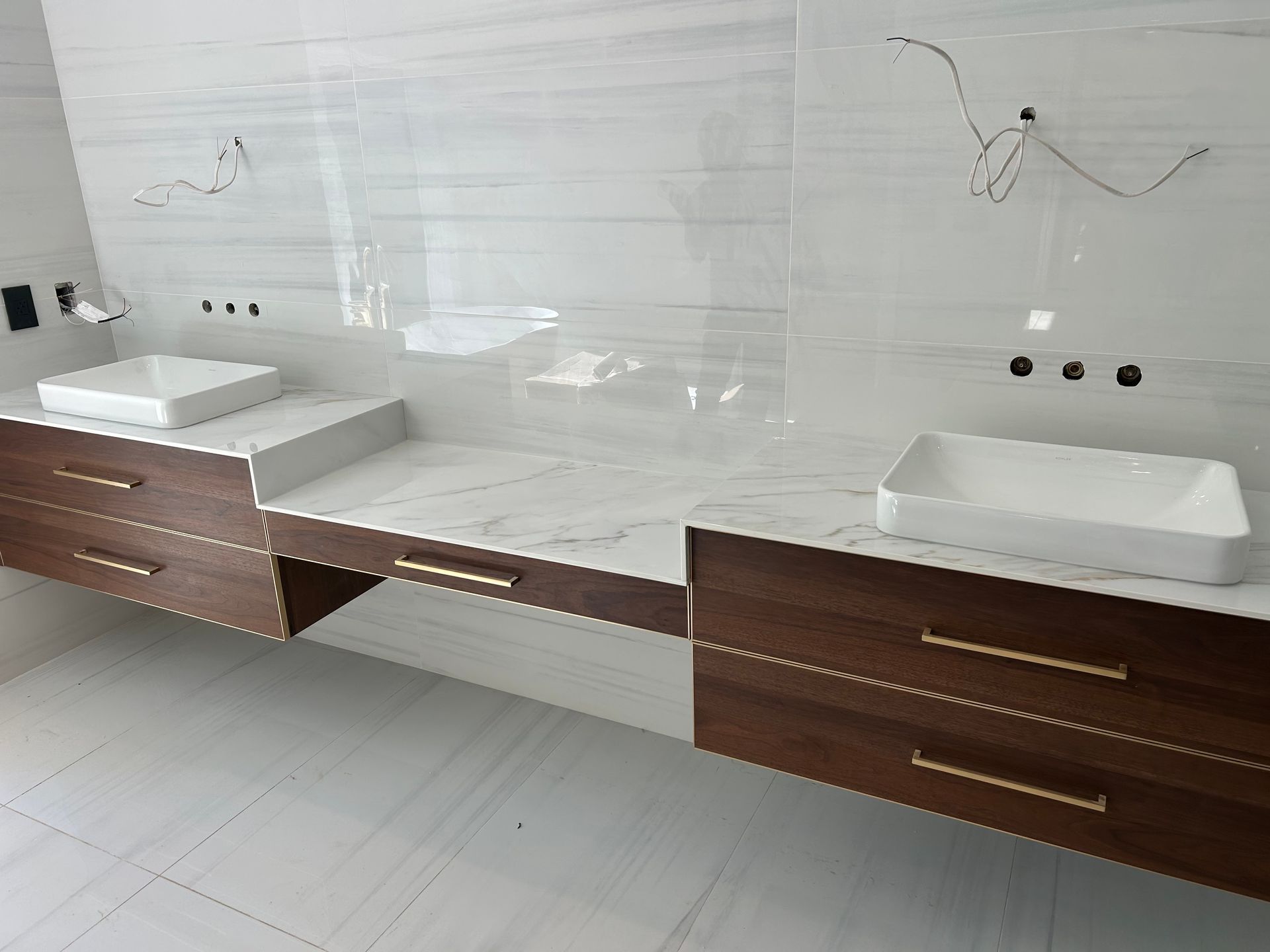 Two modern bathroom vanities with floating wood cabinets, marble countertops, and white sinks.