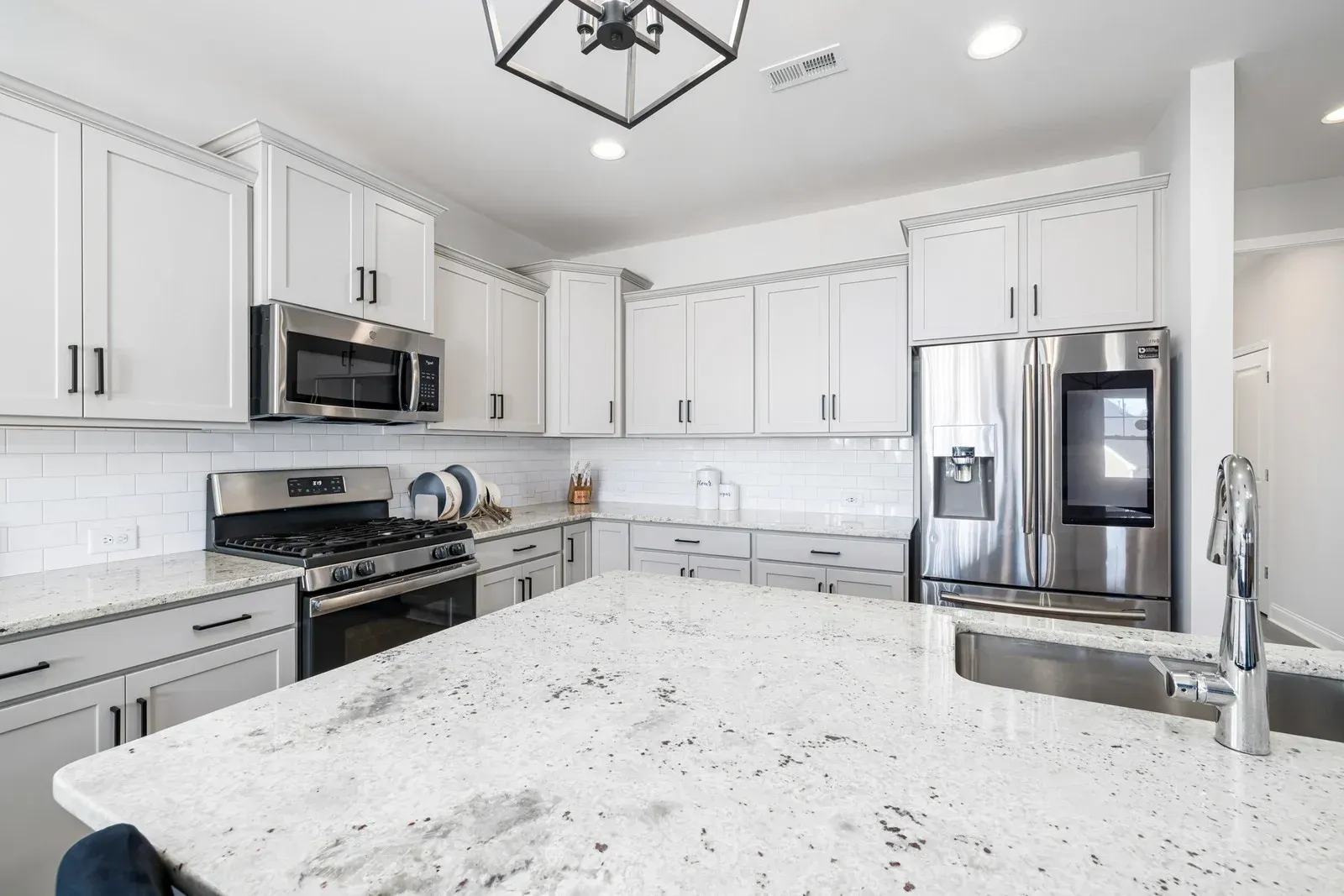 A kitchen with white cabinets , granite counter tops , stainless steel appliances and a large island.