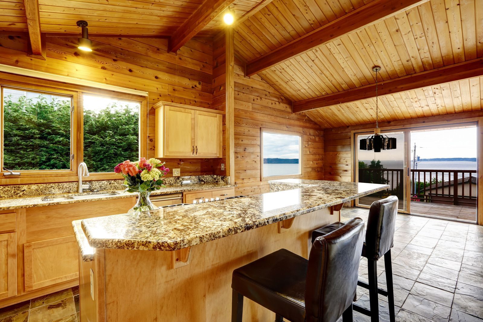 Wooden kitchen with granite countertops, bar stools, and a view of water through sliding doors.