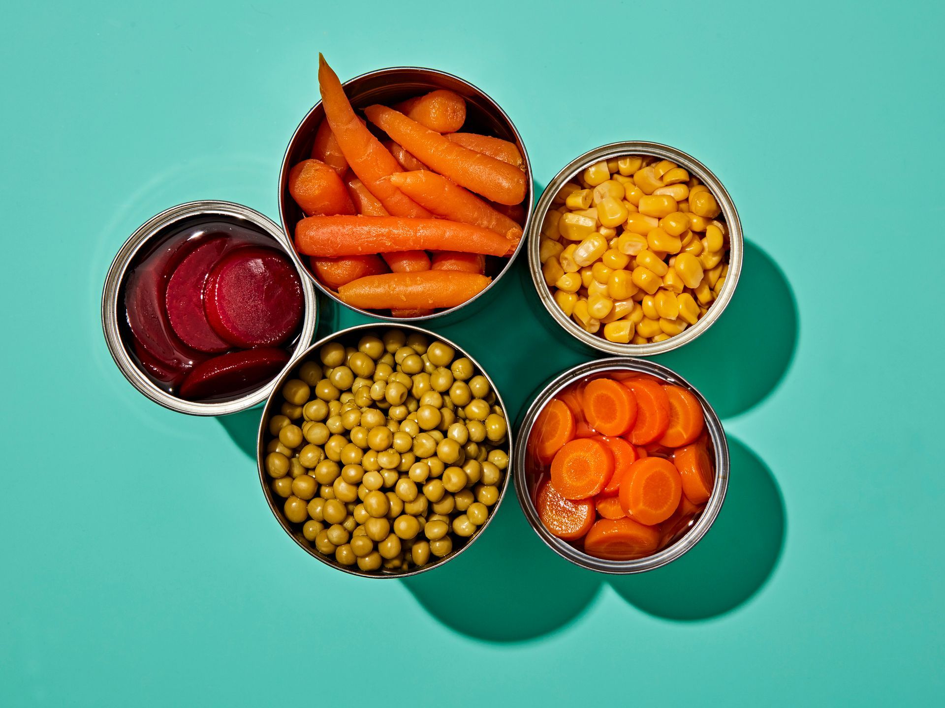 Cinque lattine aperte di verdure: barbabietole, carote, mais, piselli e carote a fette.