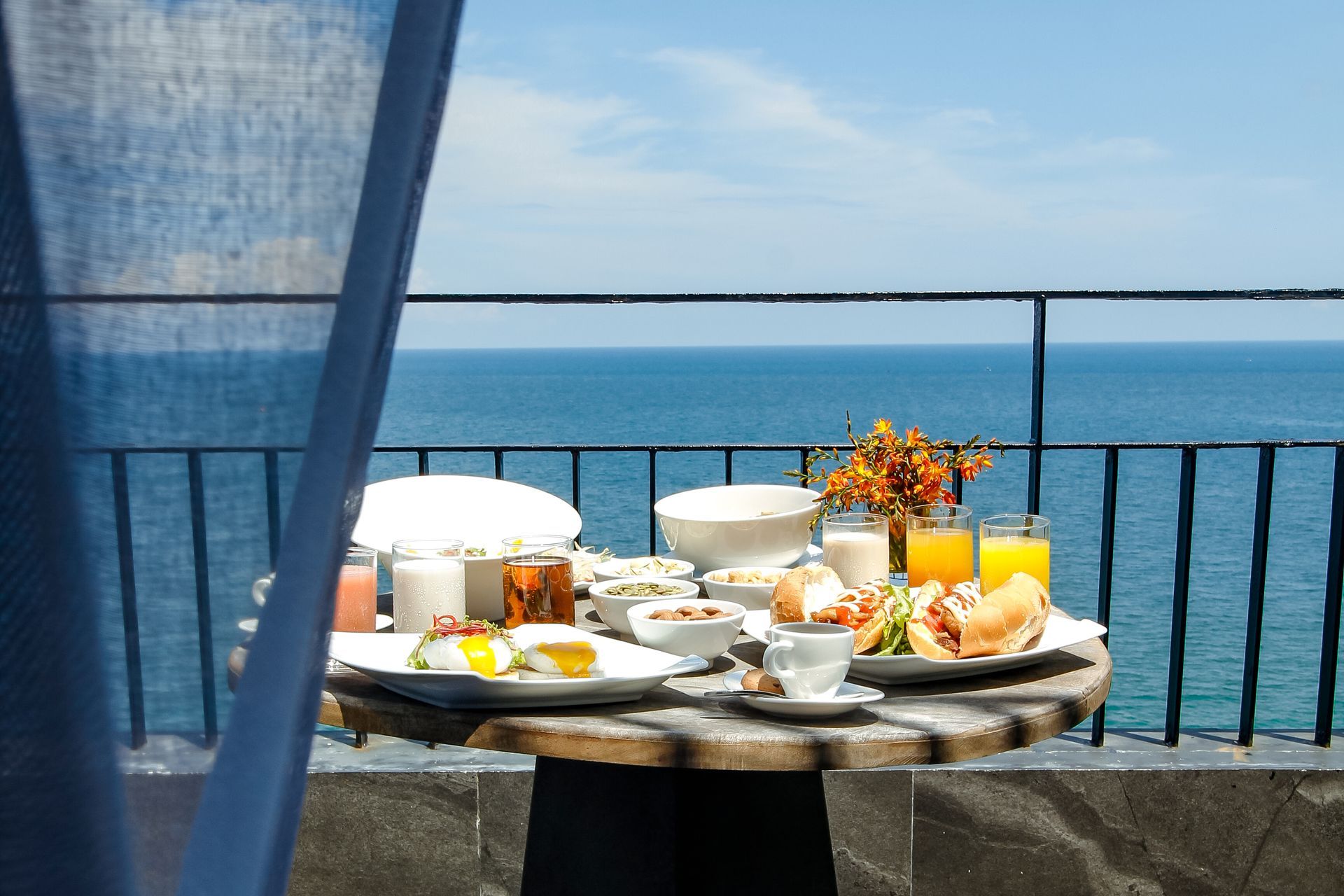 Colazione su un balcone con vista sull'oceano: cibo, bevande, fiori, giornata di sole.