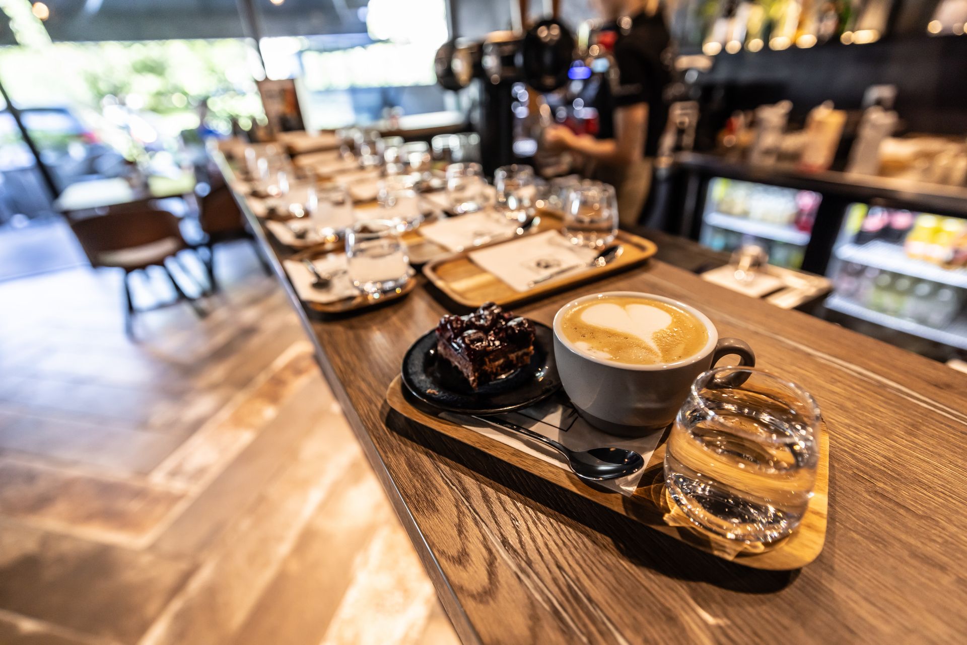 Tazza di latte, dessert e acqua su un vassoio di legno al bancone di un bar.