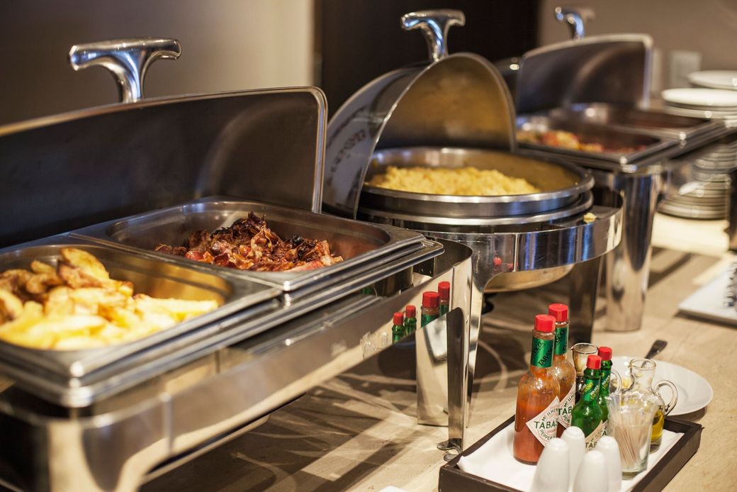 Buffet con vari piatti caldi serviti in scaldavivande d'argento. Include patate, carne e contorni.