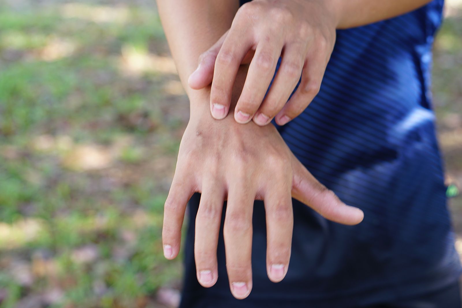 Persona que se rasca la muñeca, posiblemente debido a picazón o irritación de la piel, al aire libre.
