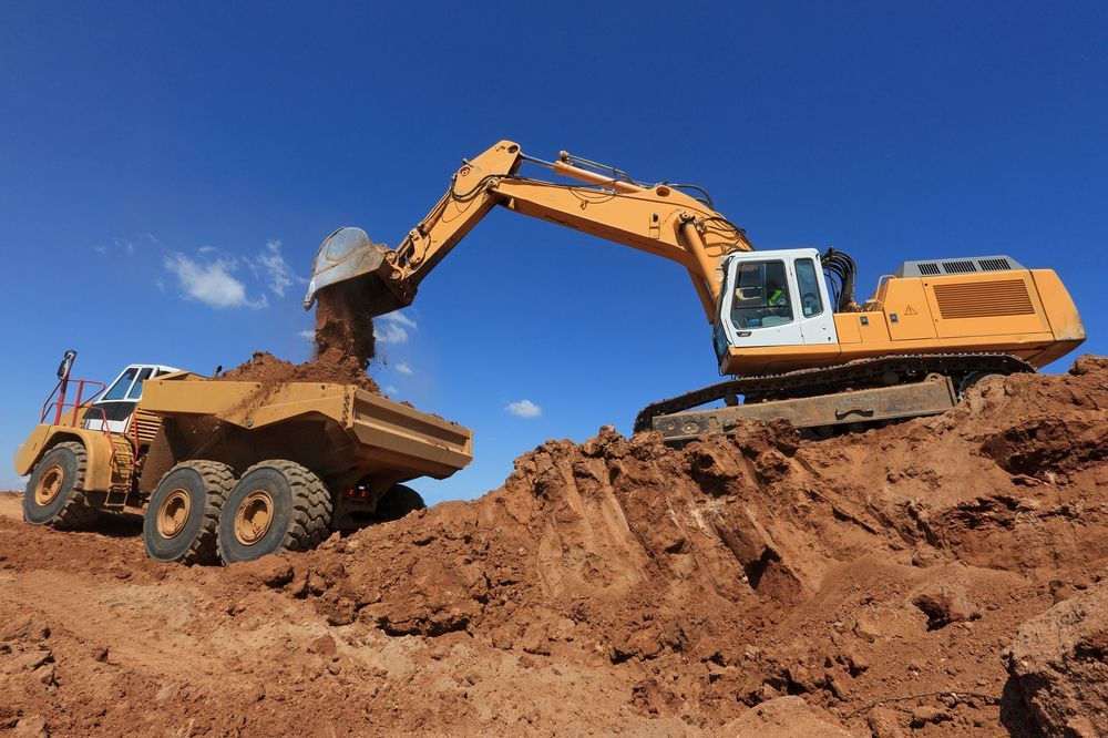 A Bulldozer is Loading Dirt Into a Dump Truck — Dino's Bobcat–Bitumen & Excavator Hire in Gayndah, QLD