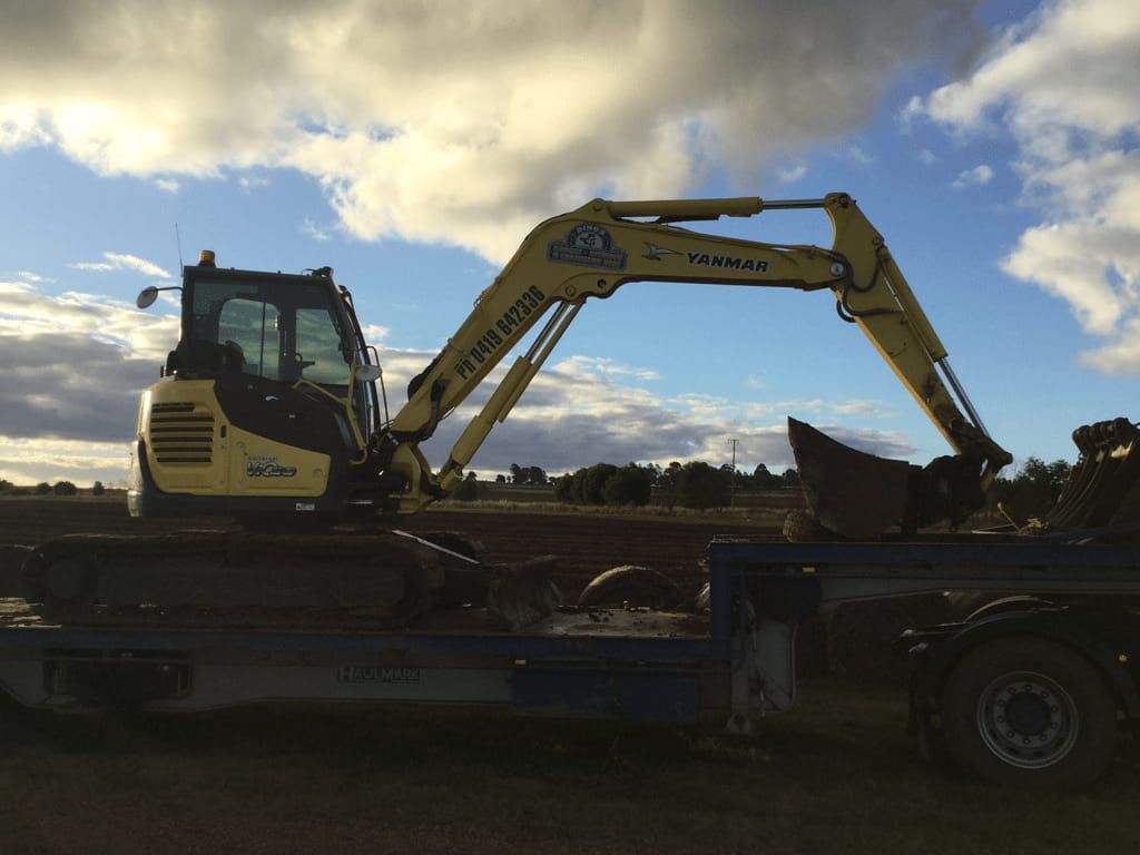 A Yellow Excavator is Parked on the Back of a Truck — Dino's Bobcat–Bitumen & Excavator Hire in Cushnie, QLD