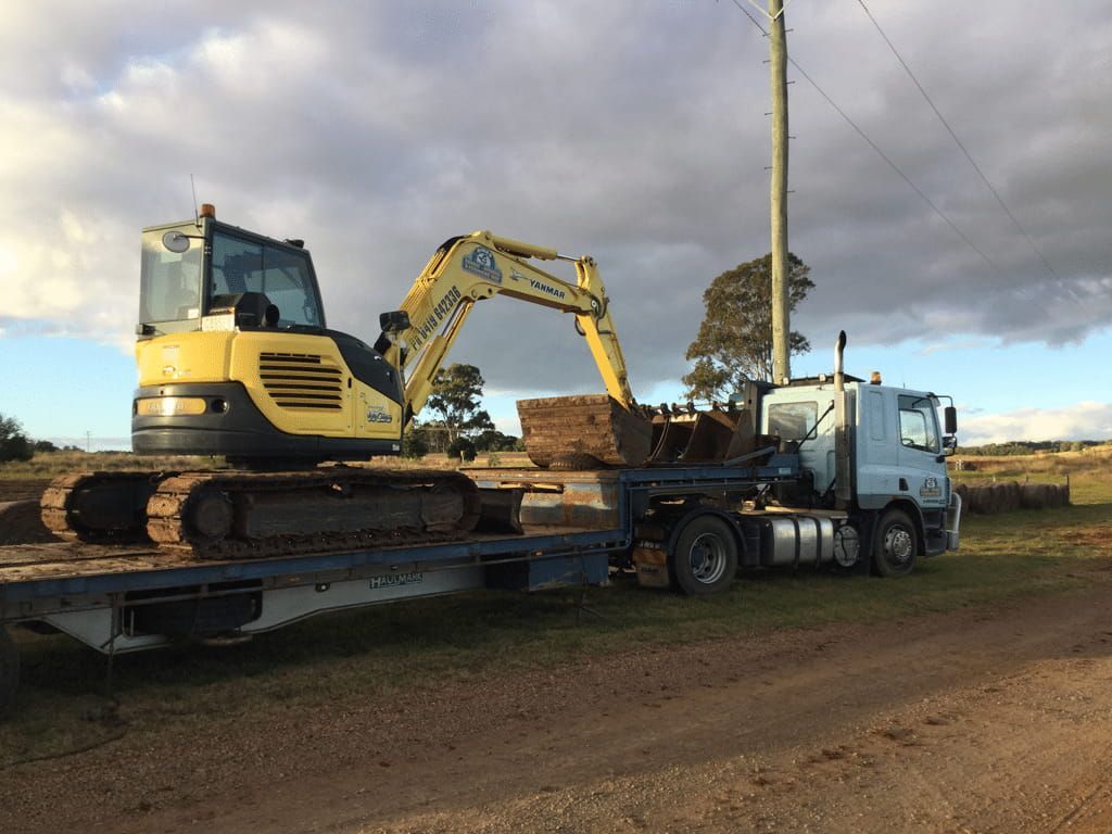 A Yellow Excavator is Sitting on Top of a Flatbed Truck — Dino's Bobcat–Bitumen & Excavator Hire in Cushnie, QLD